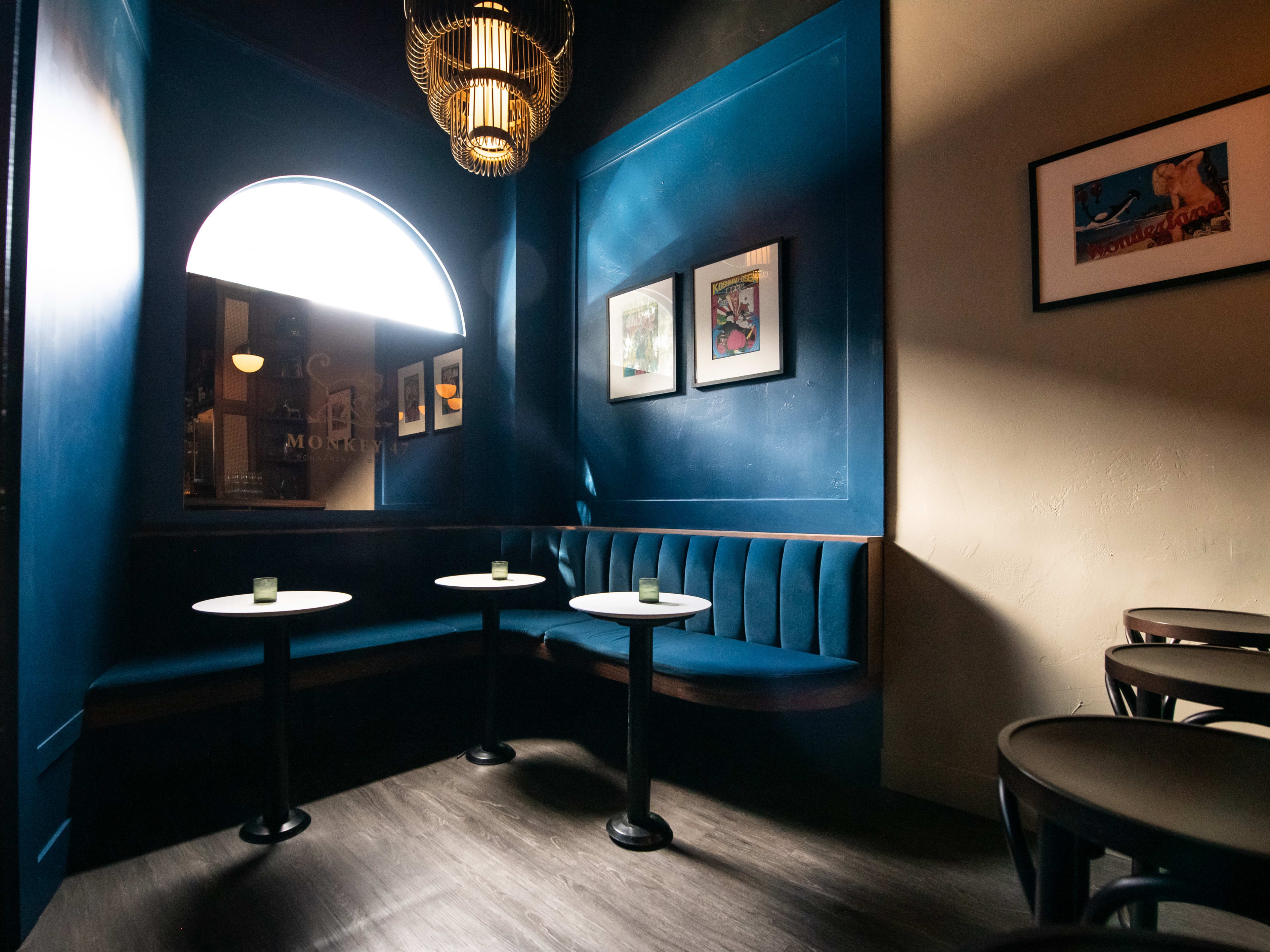 Corner of a bar with cerulean plush booths, small bistro tables, and a large mirror