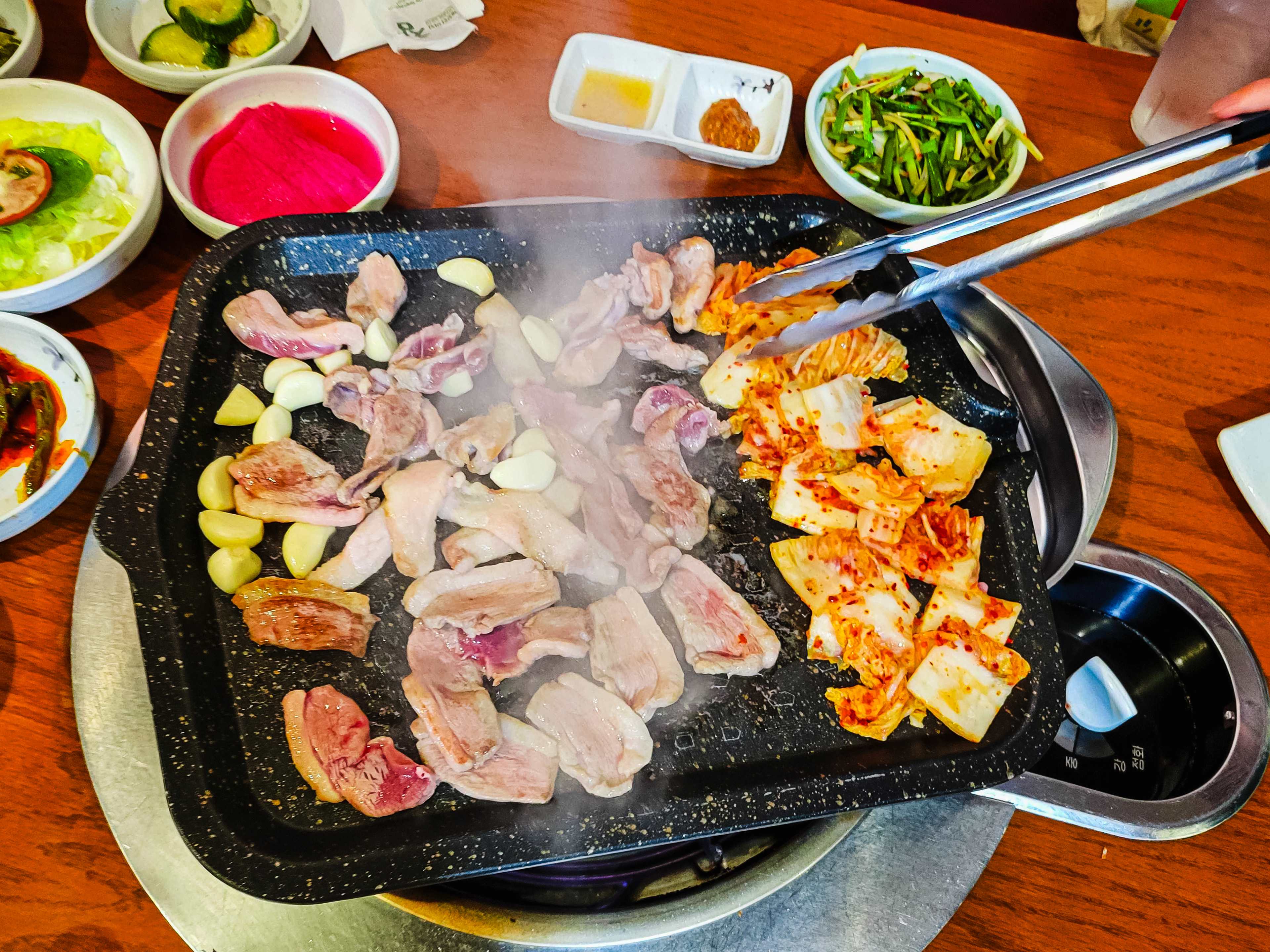 Duck and kimchi cooking on a grill in the middle of a table.