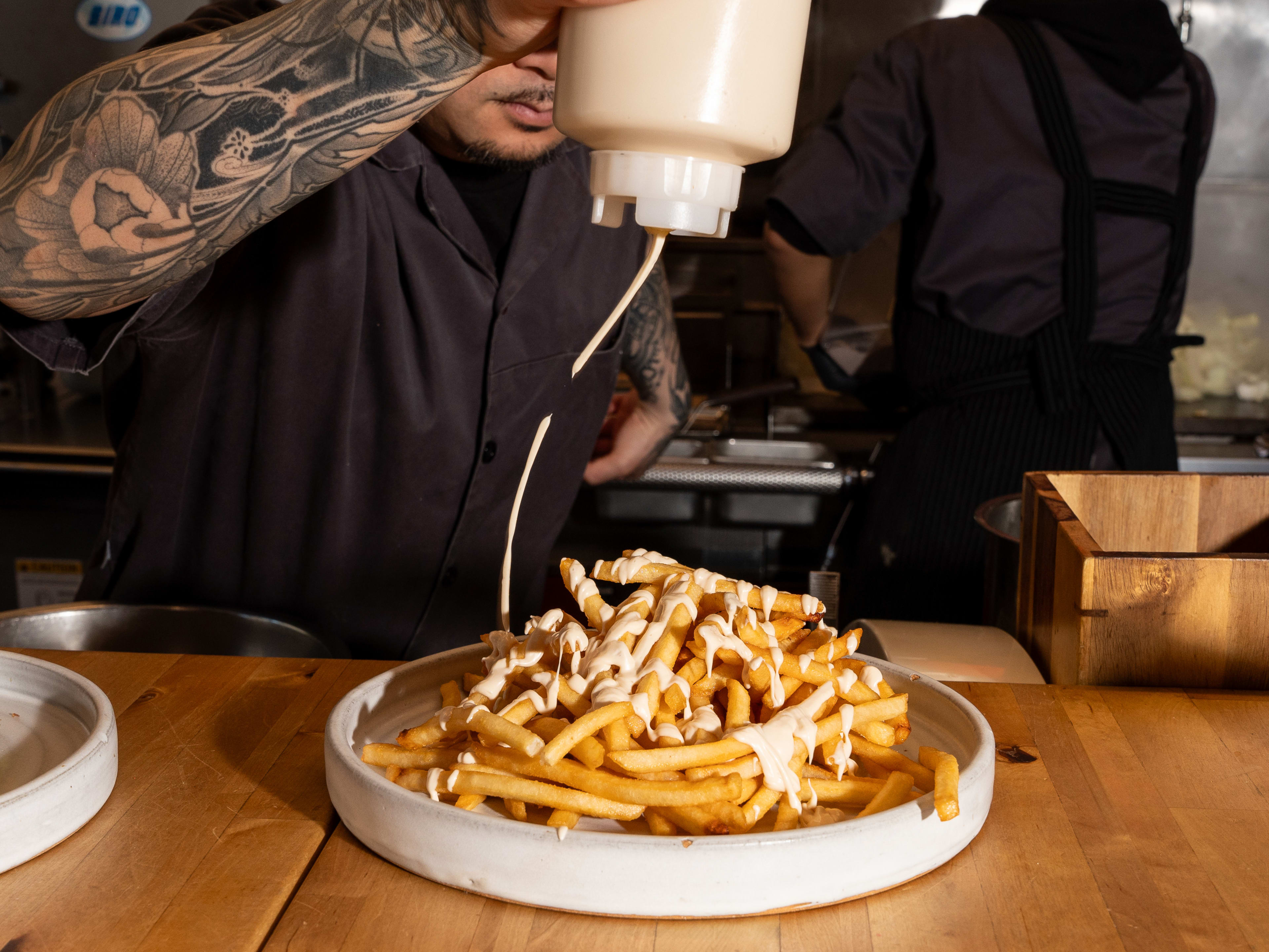 chef drizzling sauce over towering mound of fries