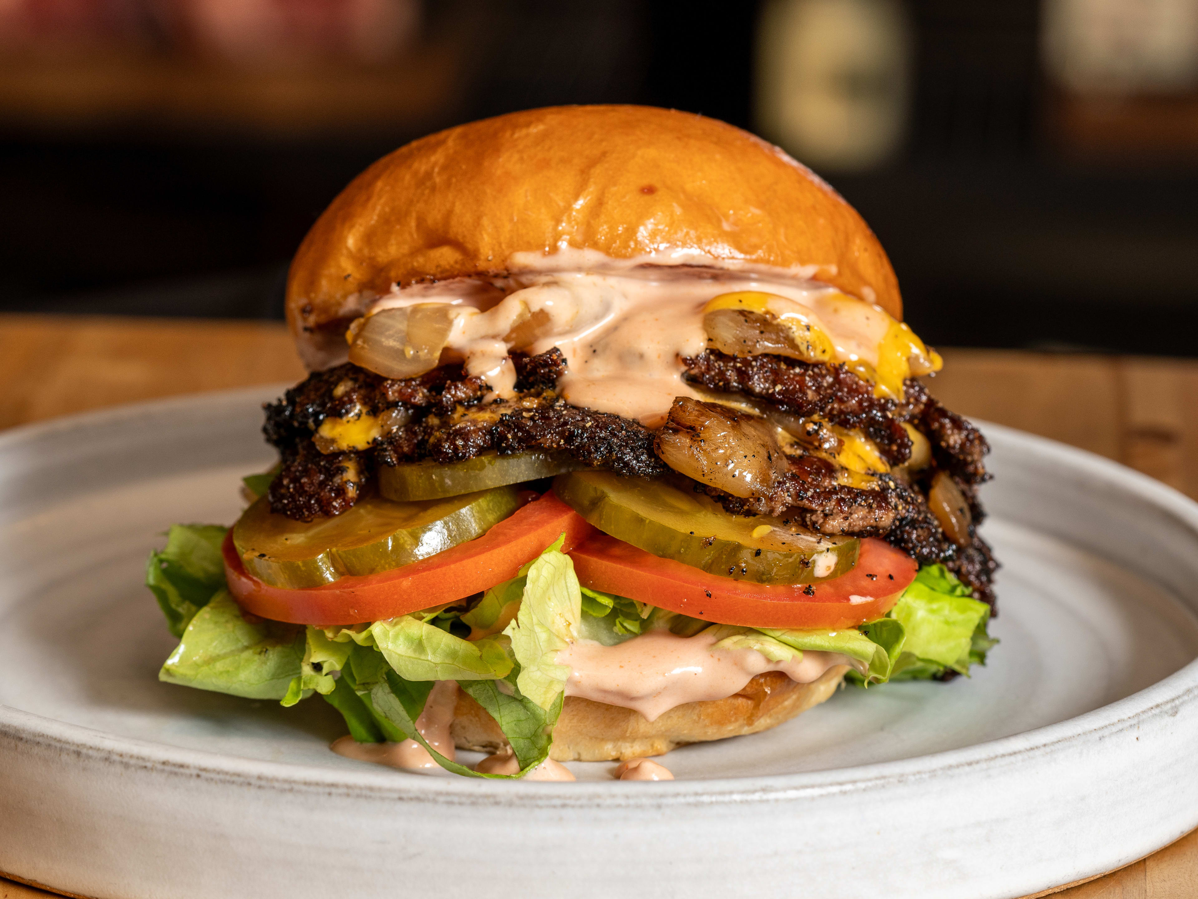 loaded smashburger with patties, cheese, sauce, tomatoes, pickles, lettuce on a bun