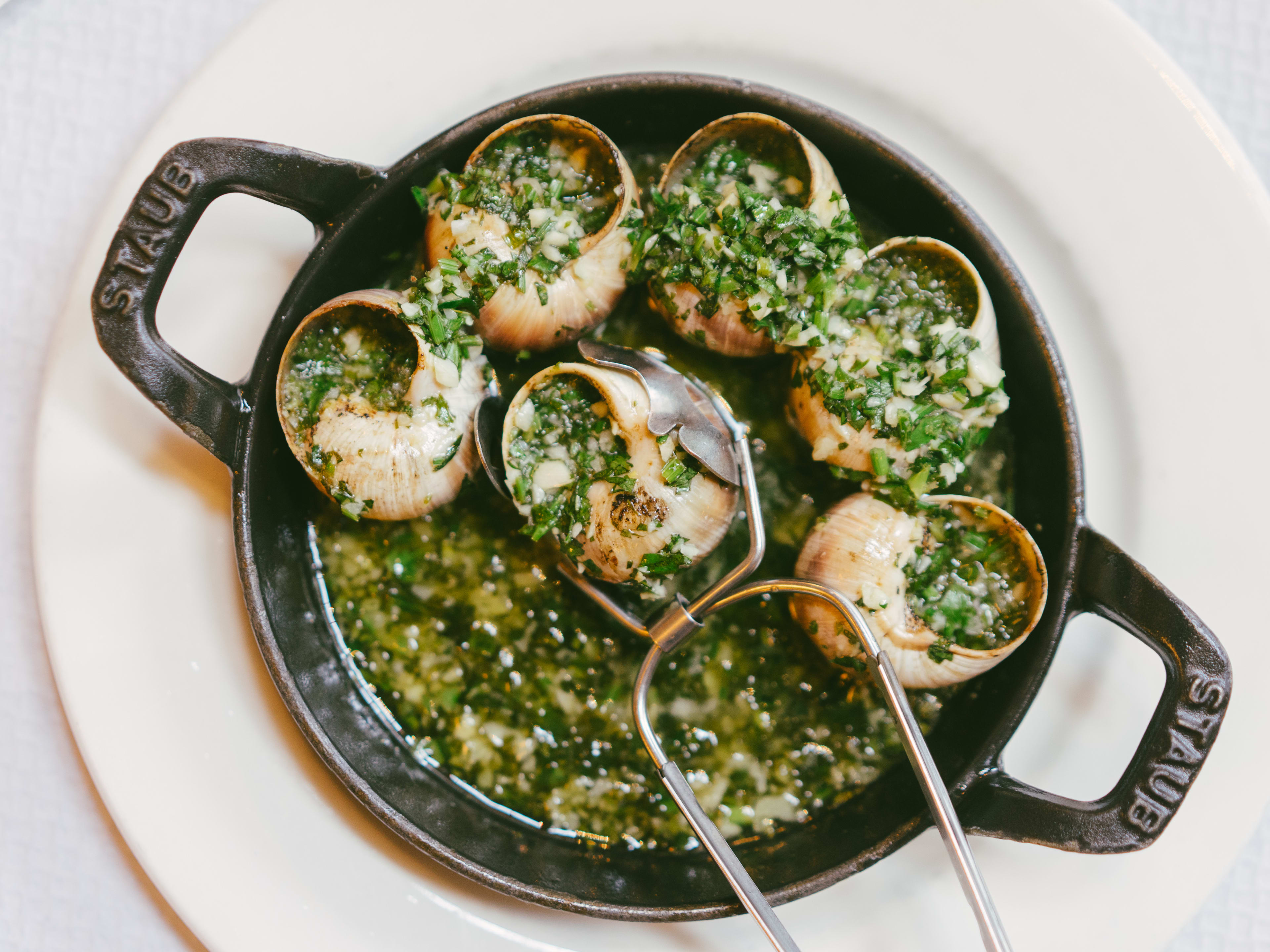 Escargots in a small cast iron dish, covered in garlic and parsley.