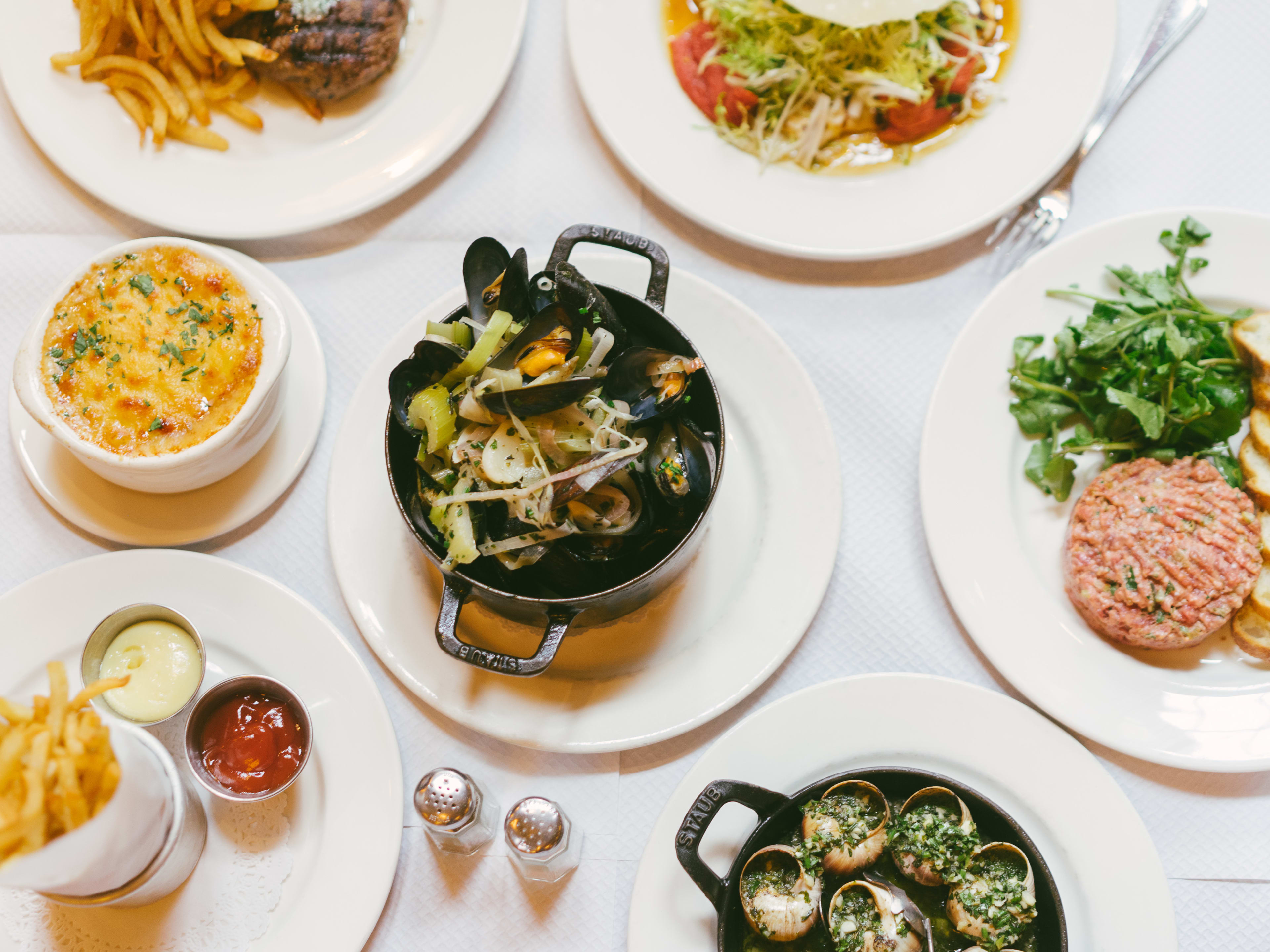 A spread of French food, including mussels, steak tartare, and French onion soup.