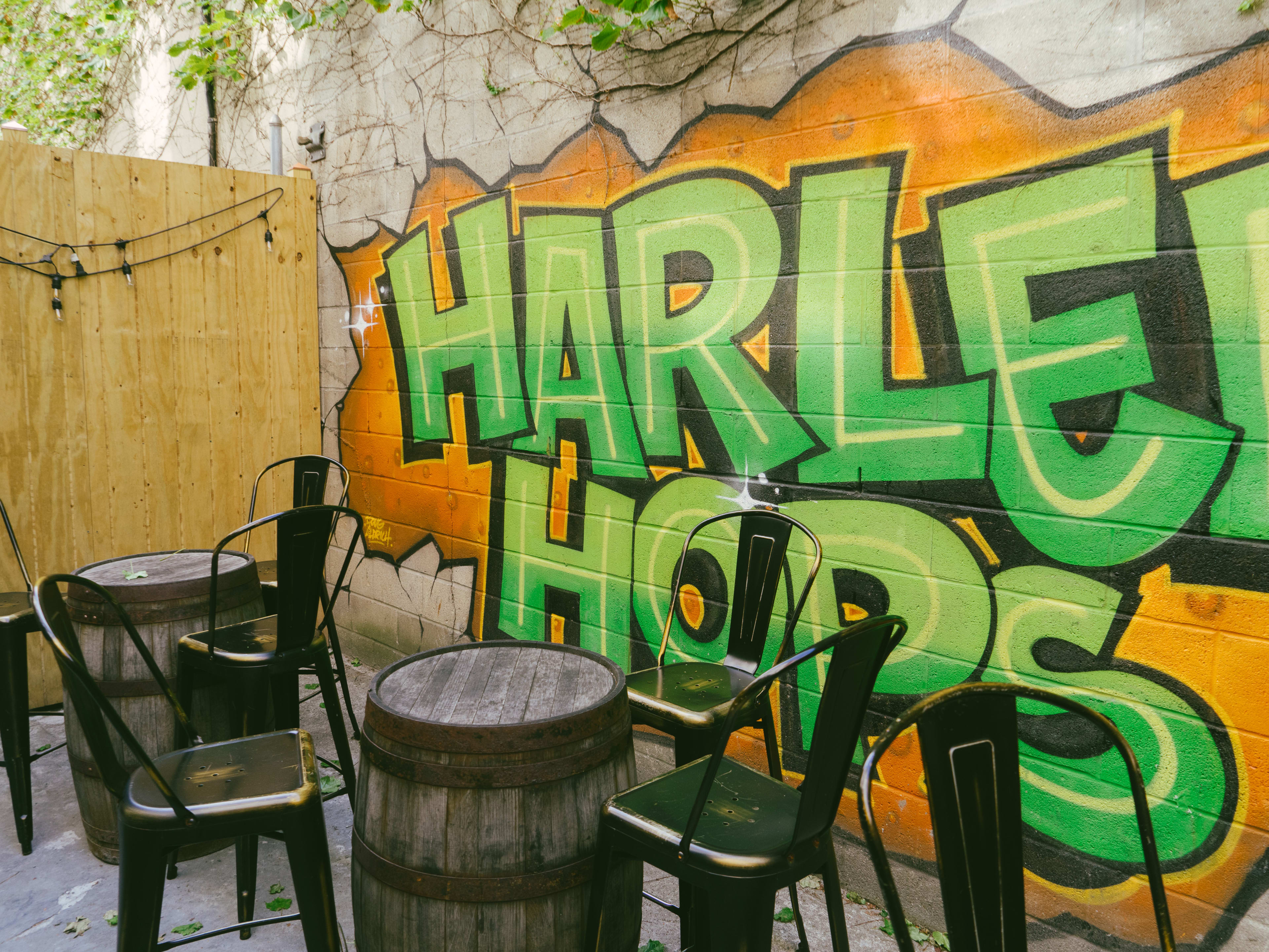 The back patio of a bar with keg tables and a mural on the wall.