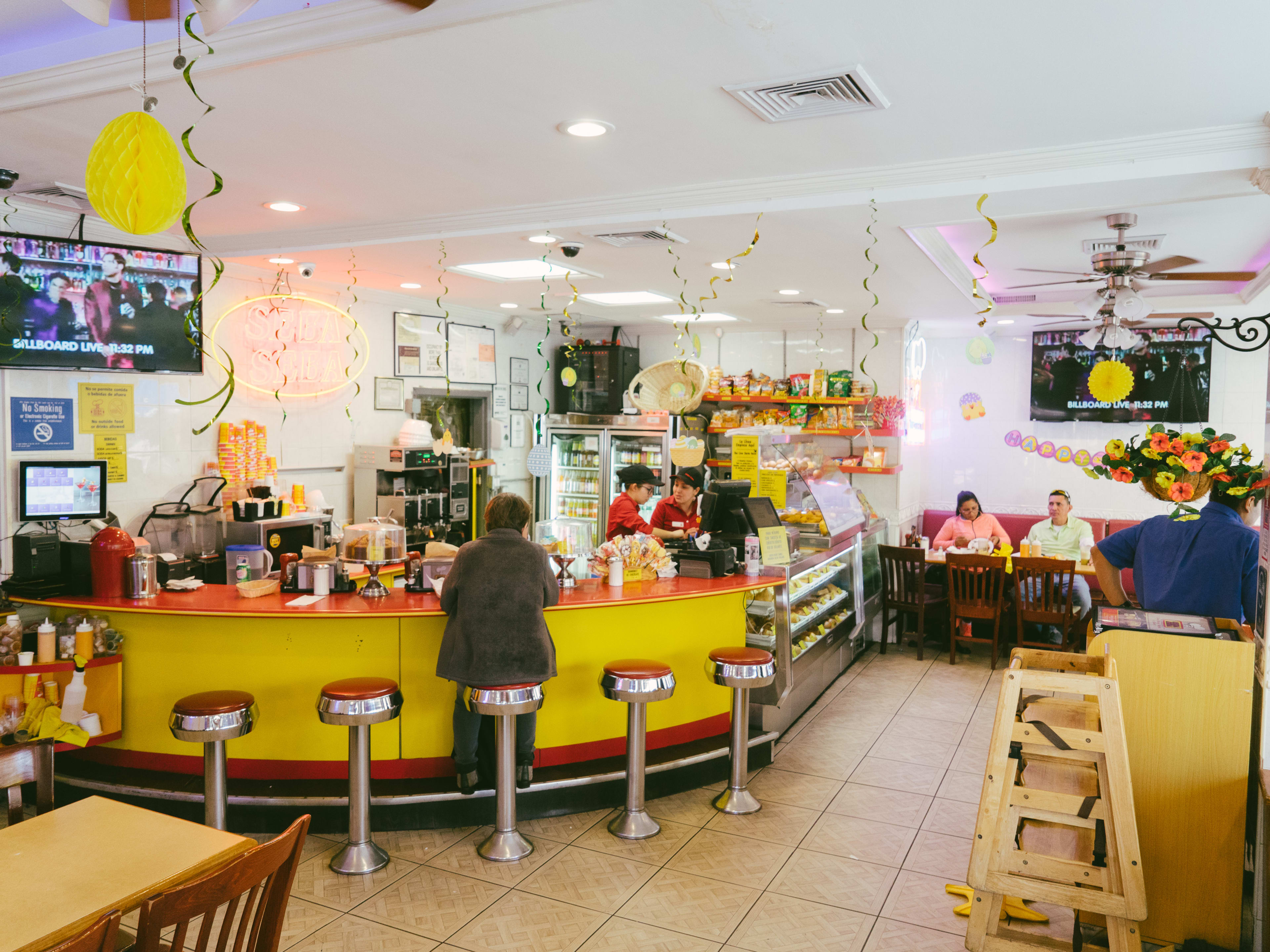 The red and yellow accented interior of Seba Seba. A person sits on a red stool at a rounded bar. And there are banquettes and other tables.