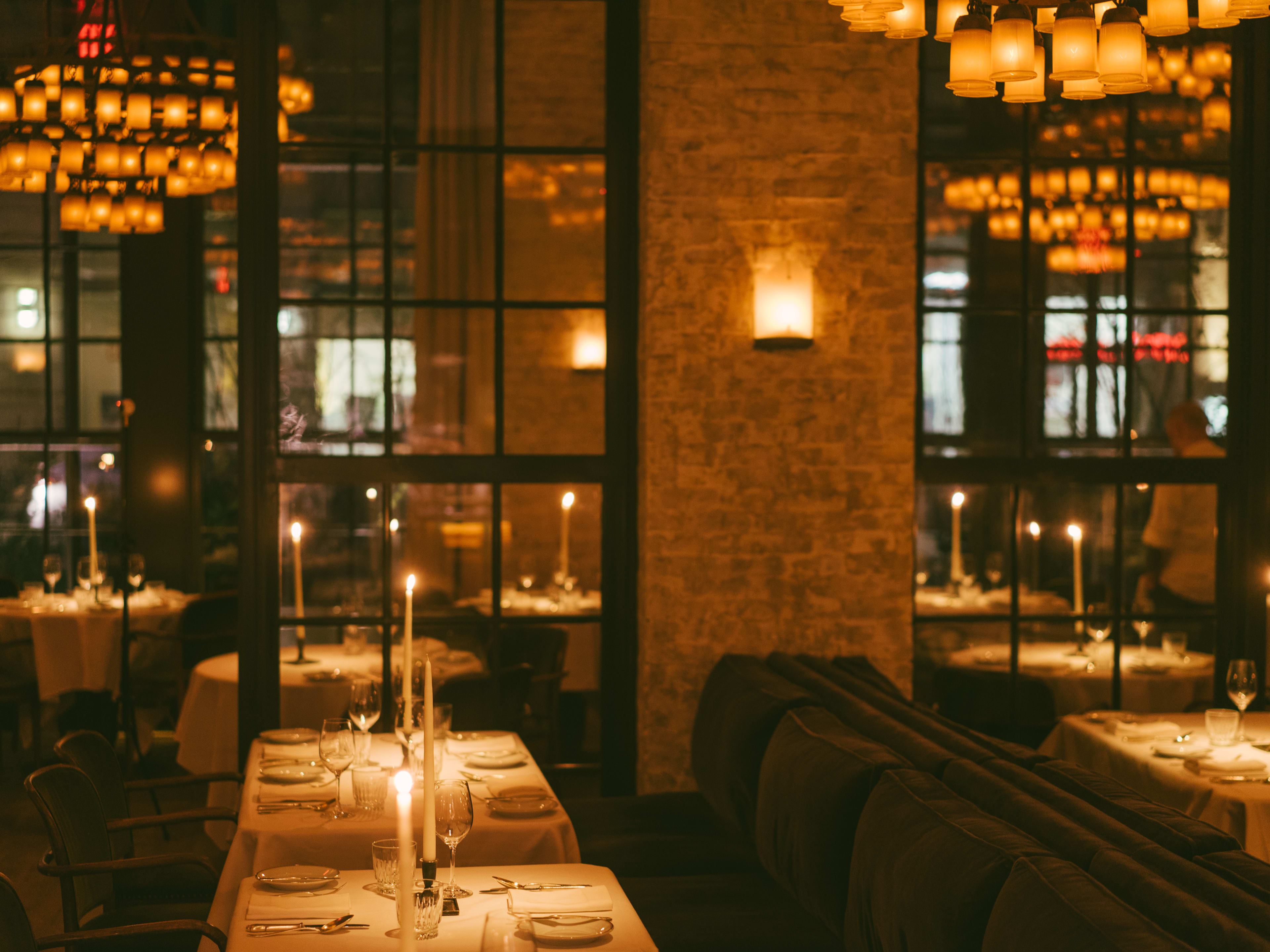 A dark restaurant with tall candles, chandeliers, and white tablecloths.