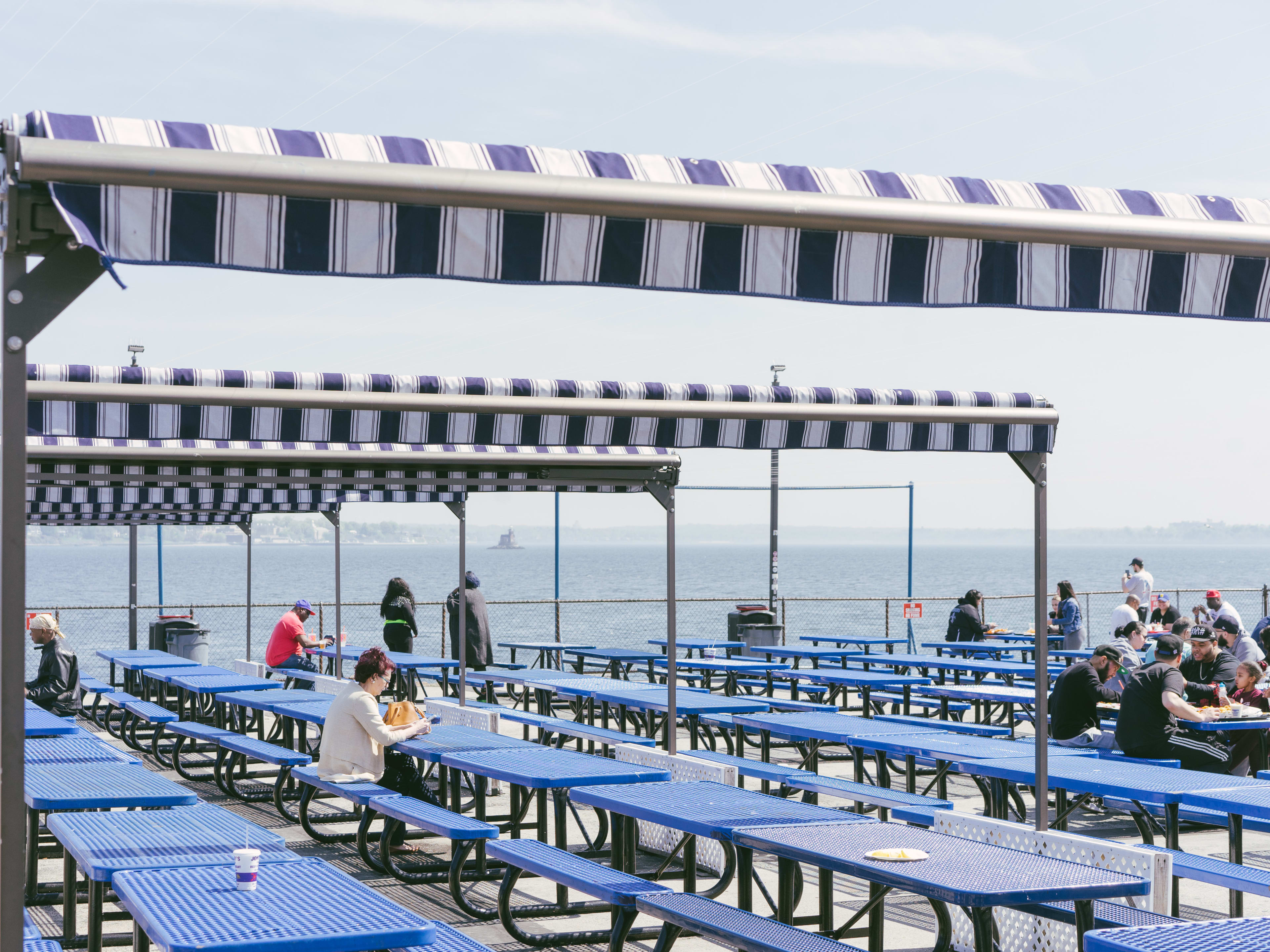 A patio covered in big blue picnic tables near the water on City Island.