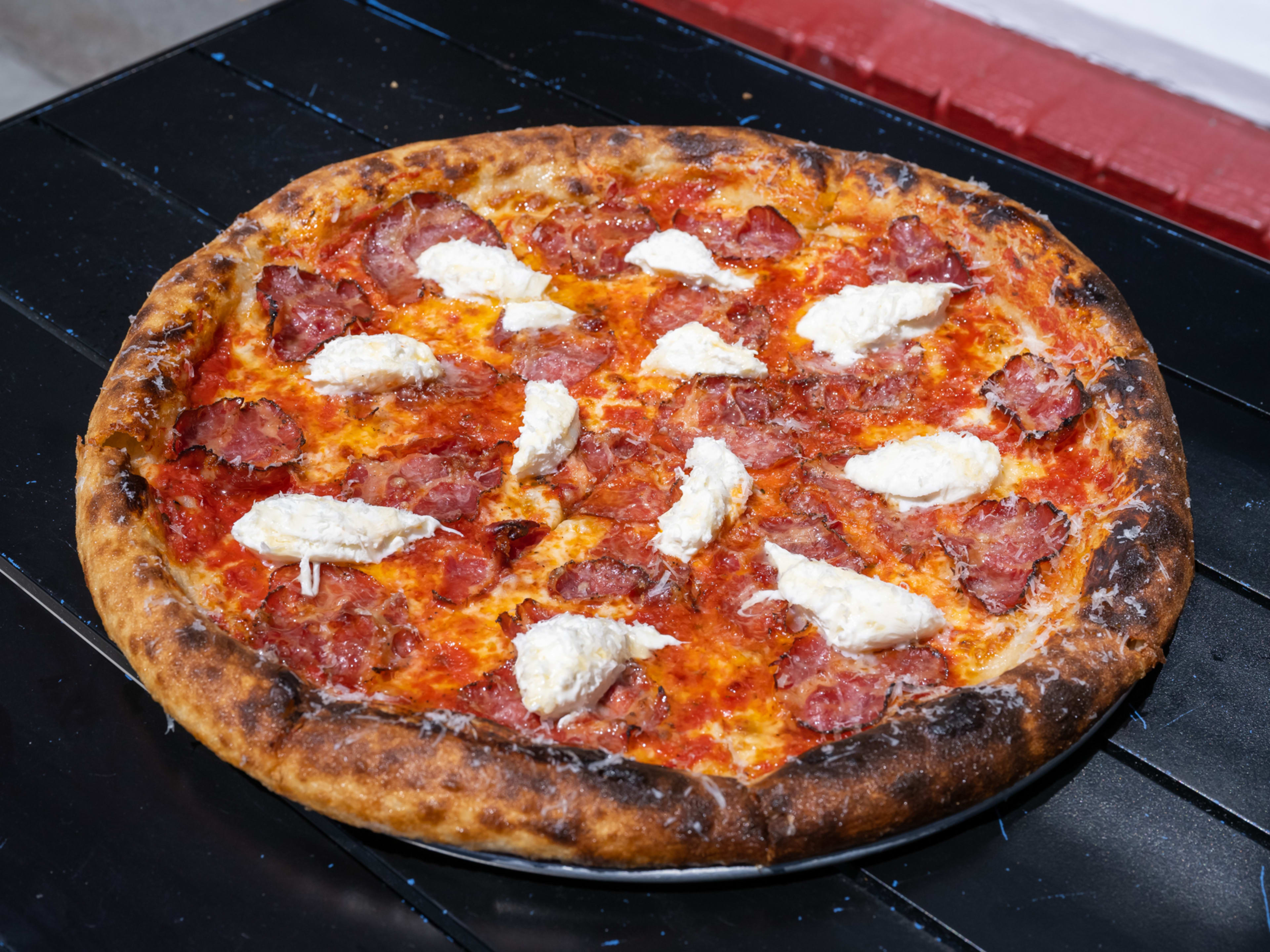 a red sauce-based pizza topped with capocollo, burrata, and a drizzle of hot honey