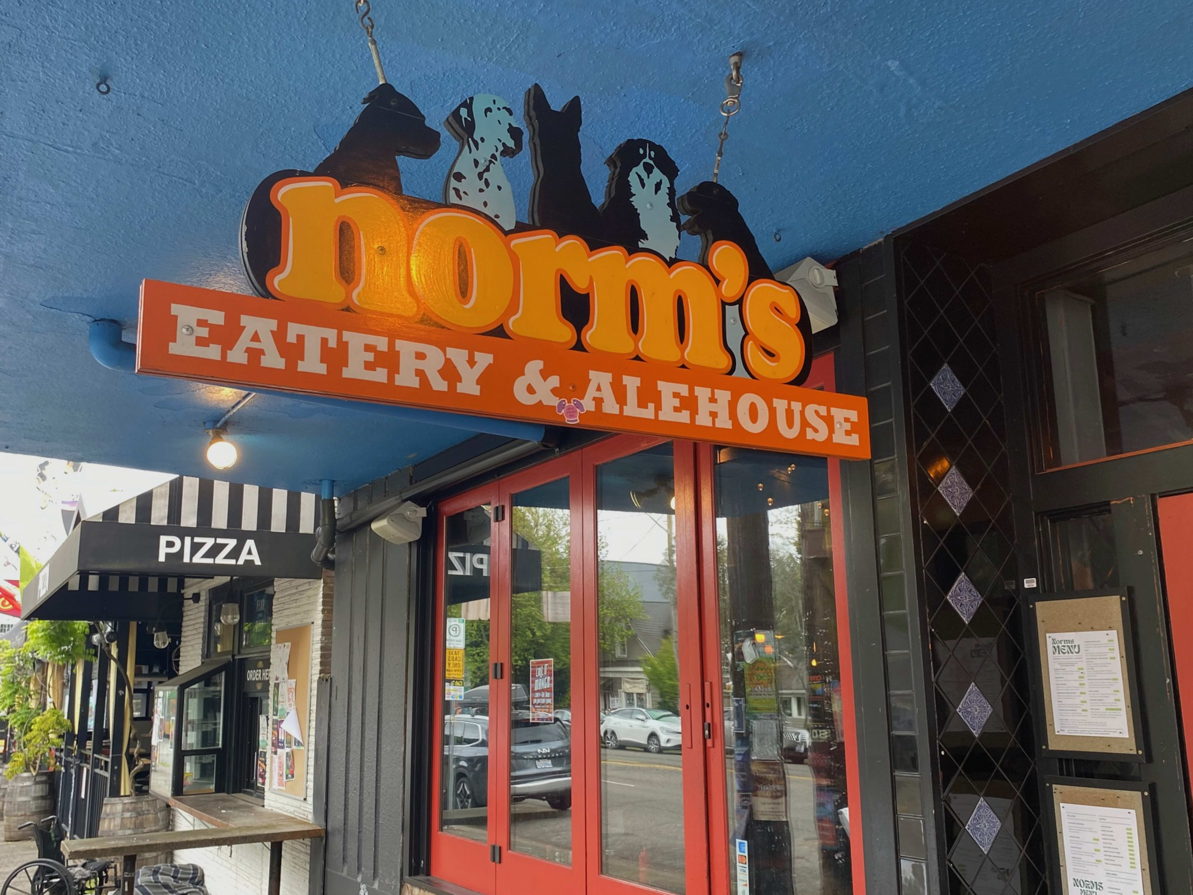 A sign in orange lettering that says "Norm's" with graphics of several dogs.