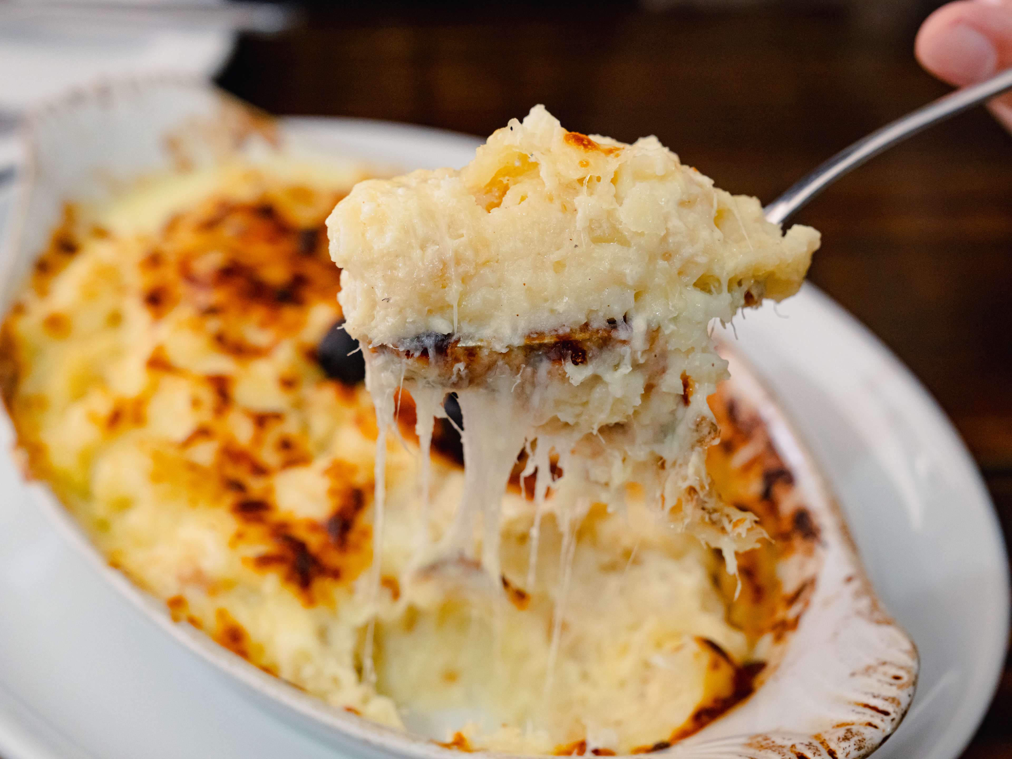 A spoon lifting up cheesy bacalhau com natas.