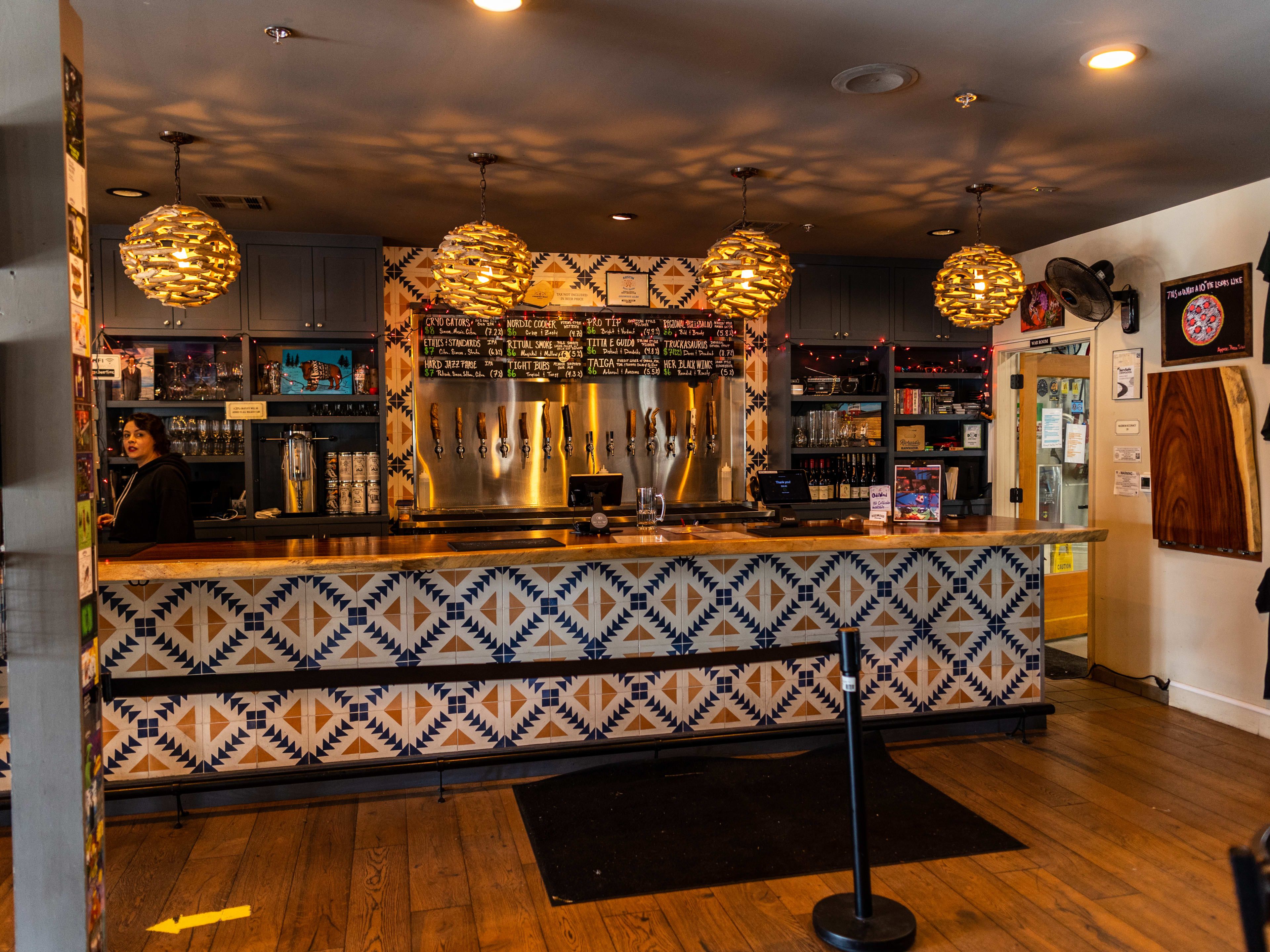 The decorative tiled bar area inside Oddwood Brewing. There are taps on the back wall and pendant lights hanging from the ceiling.