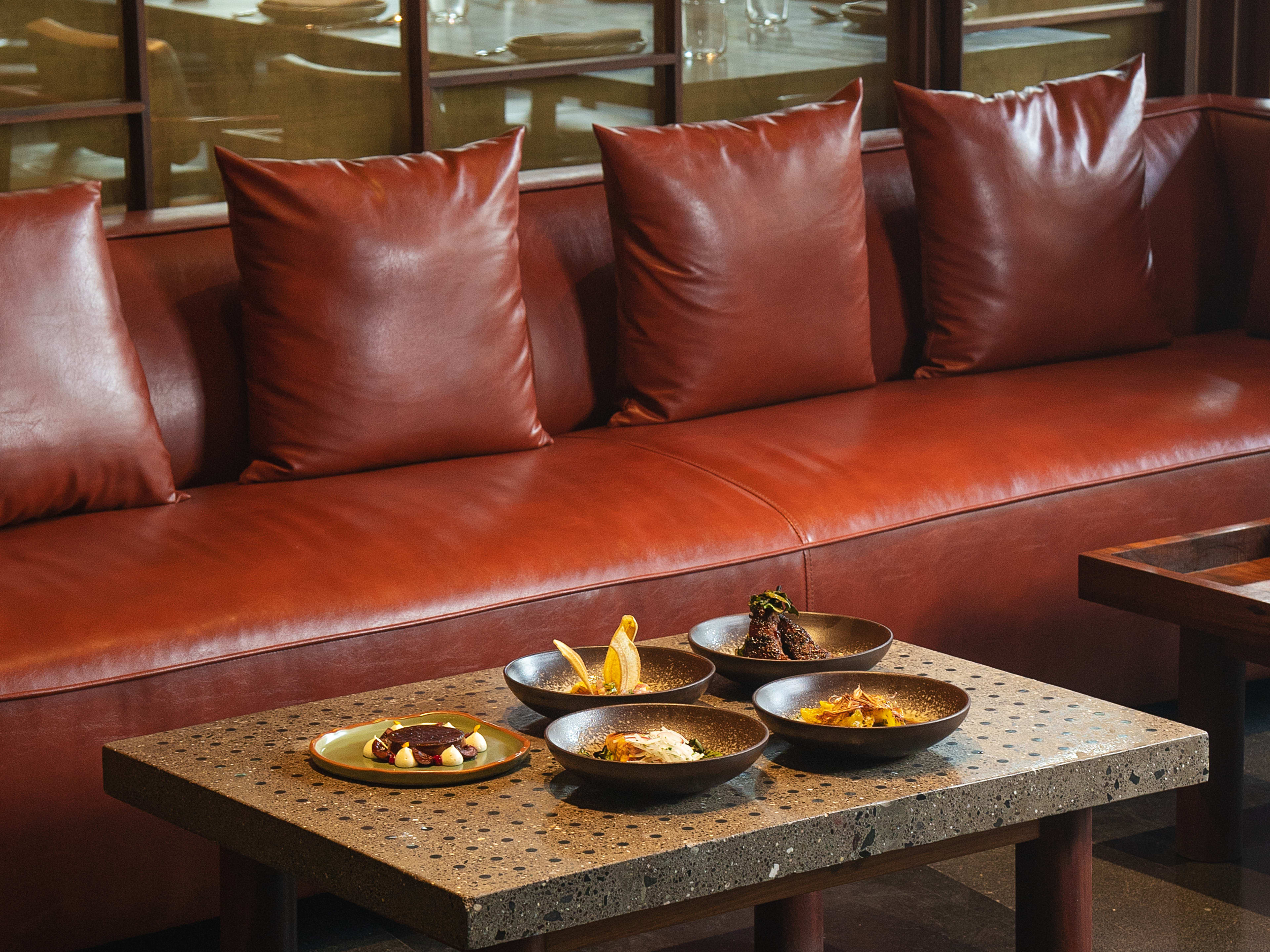 Spread of dishes on table in red leather lounge area at Ode