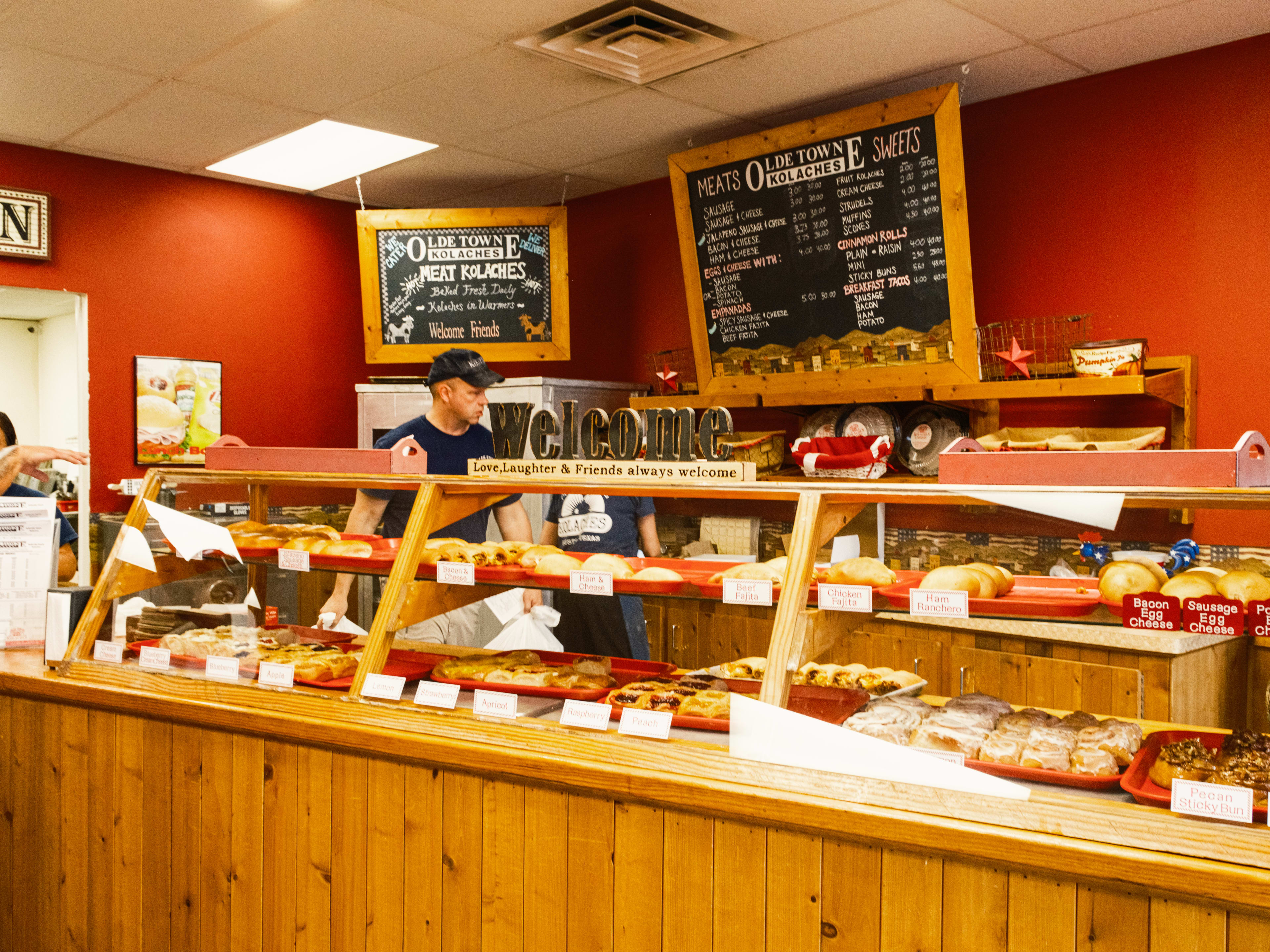 The wooden pastry case at Olde Towne Kolaches. The walls are red and there are red and white gingham accents.