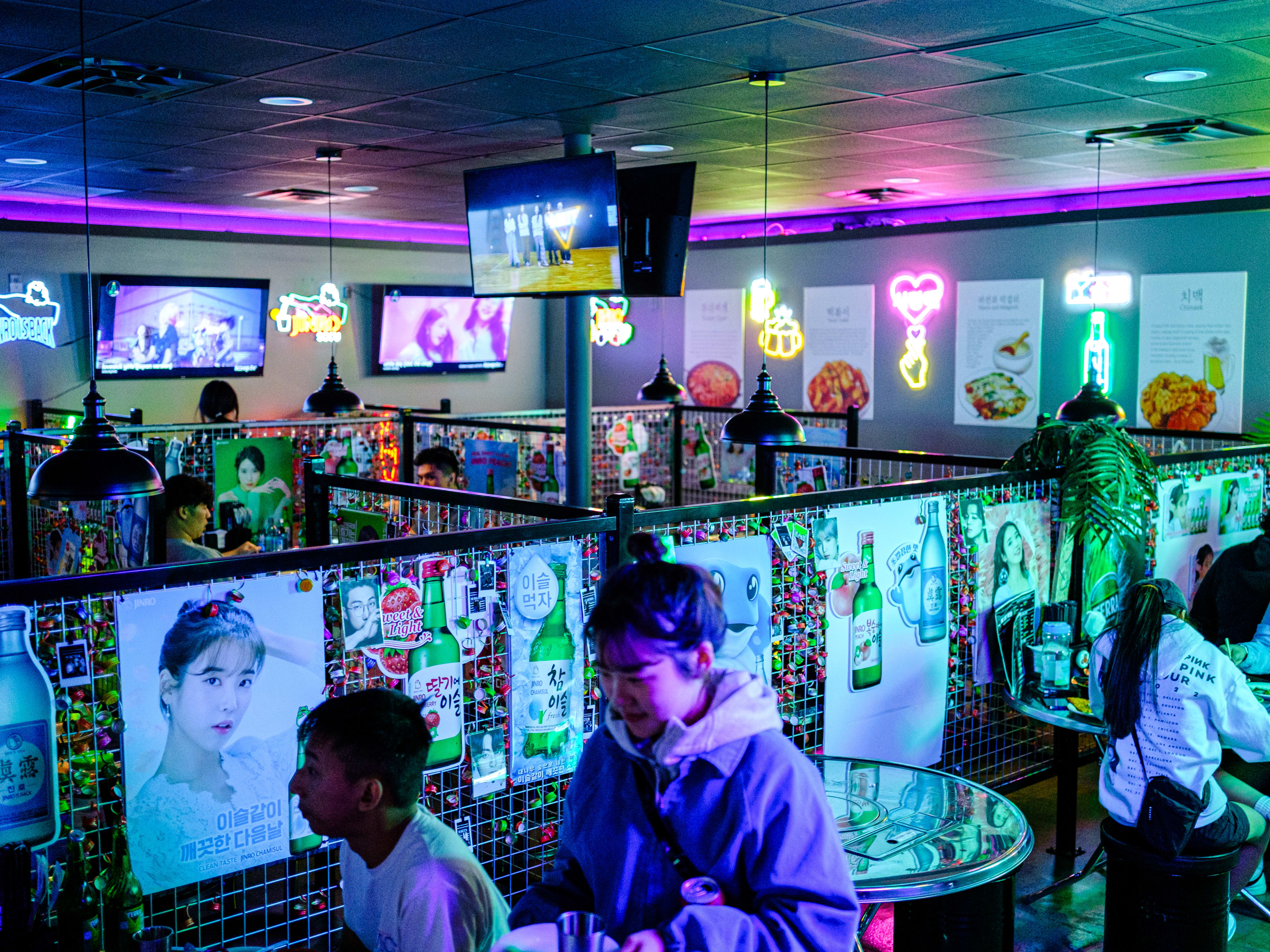 photo depicts the interior of one shot pocha, with neon signs along the wall and tables separated by chainlink dividers