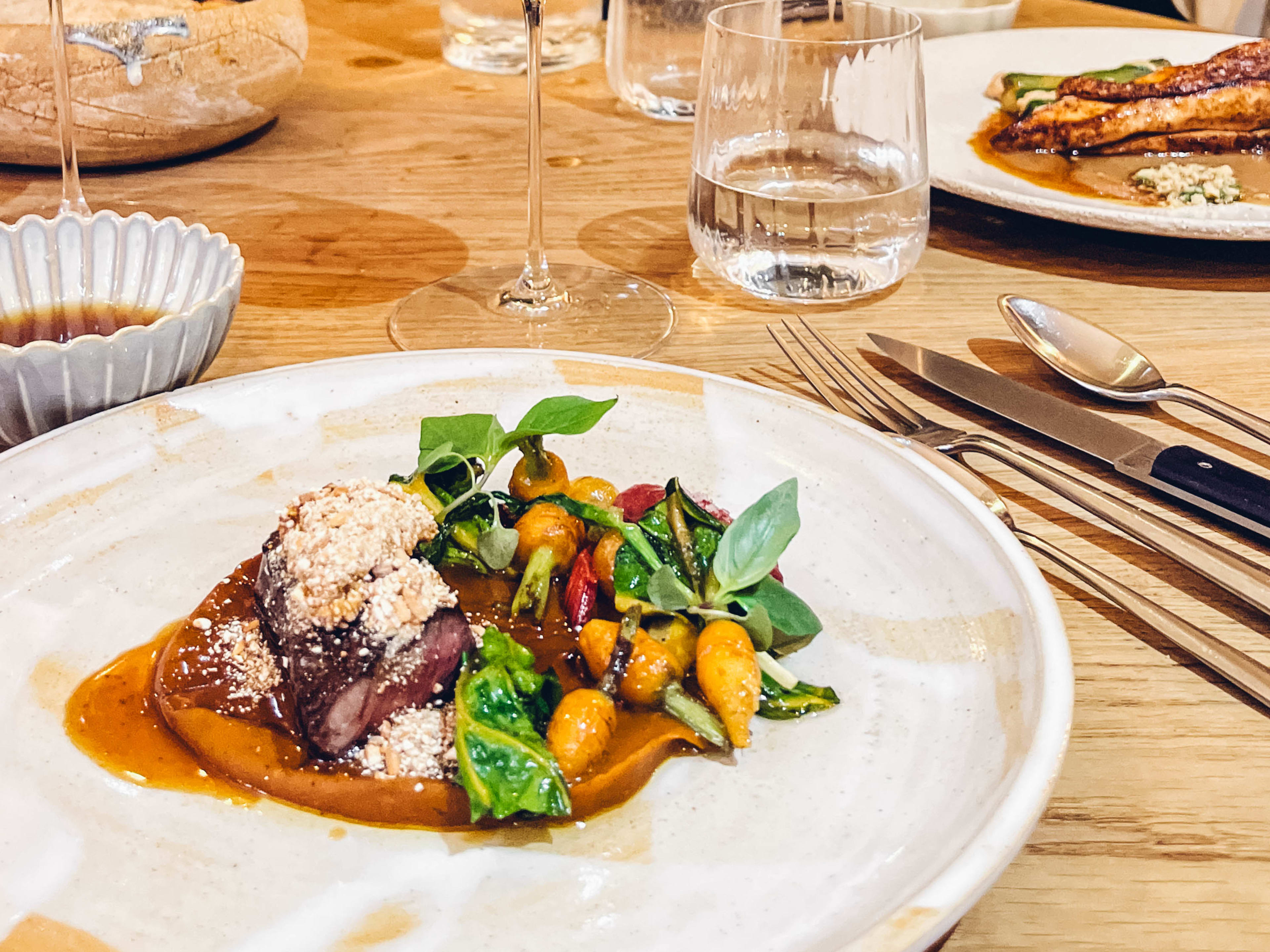 A plate of meat and vegetables on a wooden table at Ambos, a restaurant in Paris