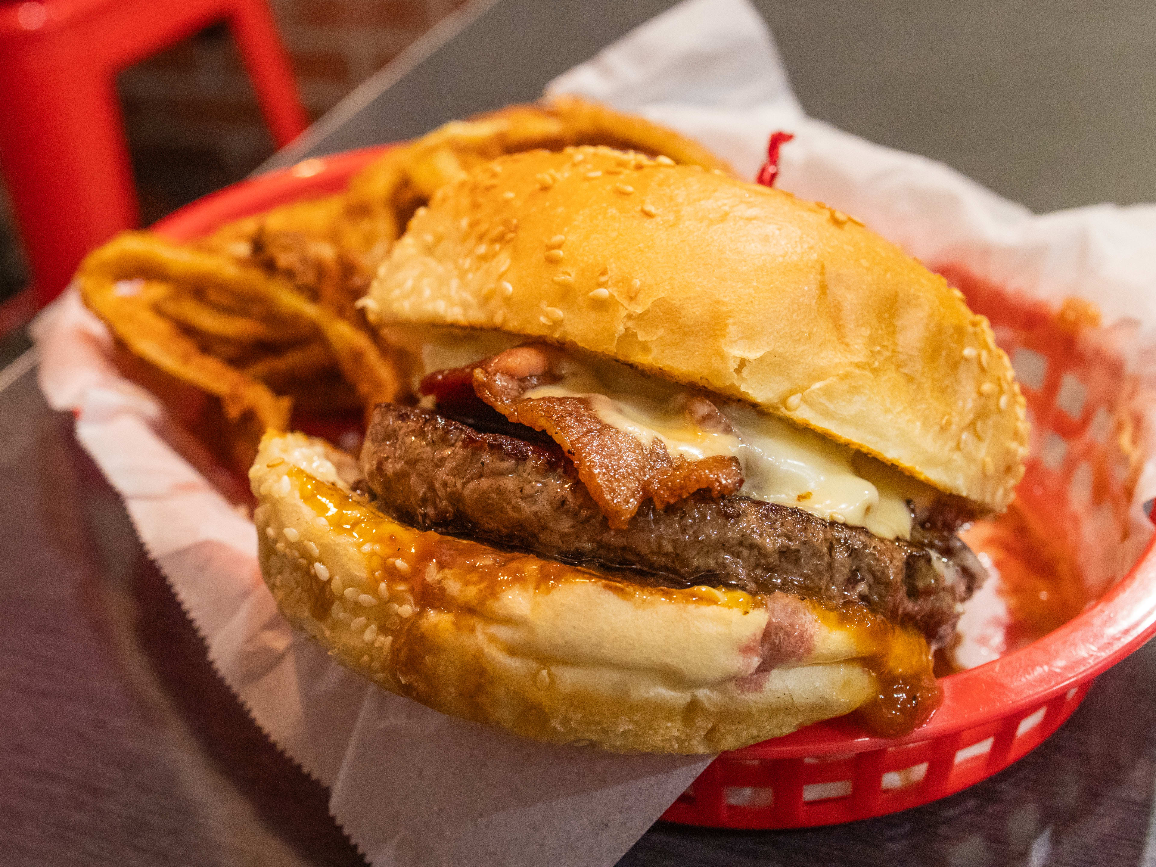 burger with tall seeded bun, patty, melty cheese, bacon, served in basket with onion rings