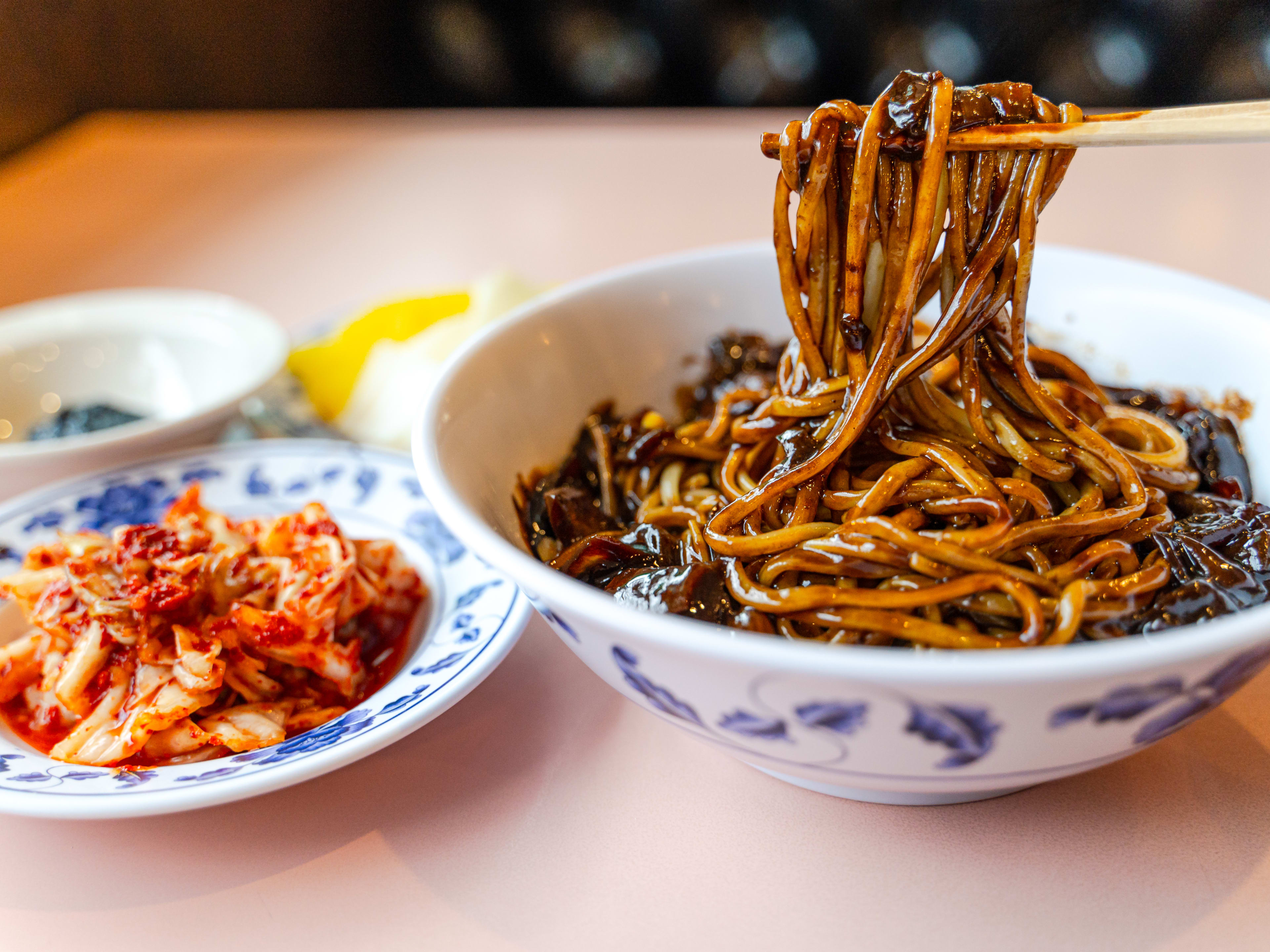 A bowl of jjajangmyeon with a side of kimchi.