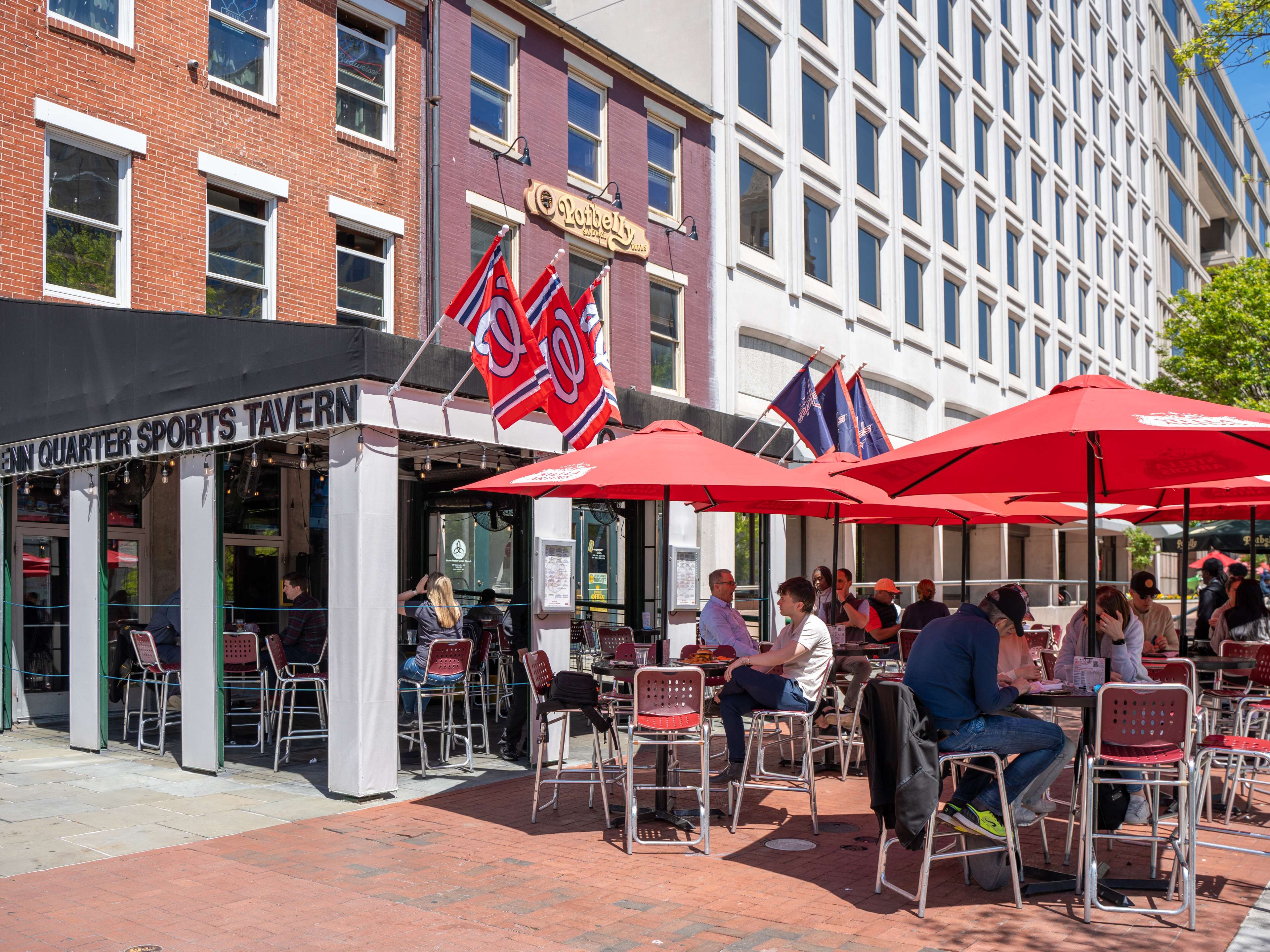 exterior of bar with DC sports flags hanging from awning and outdoor patio with tables under umbrellas