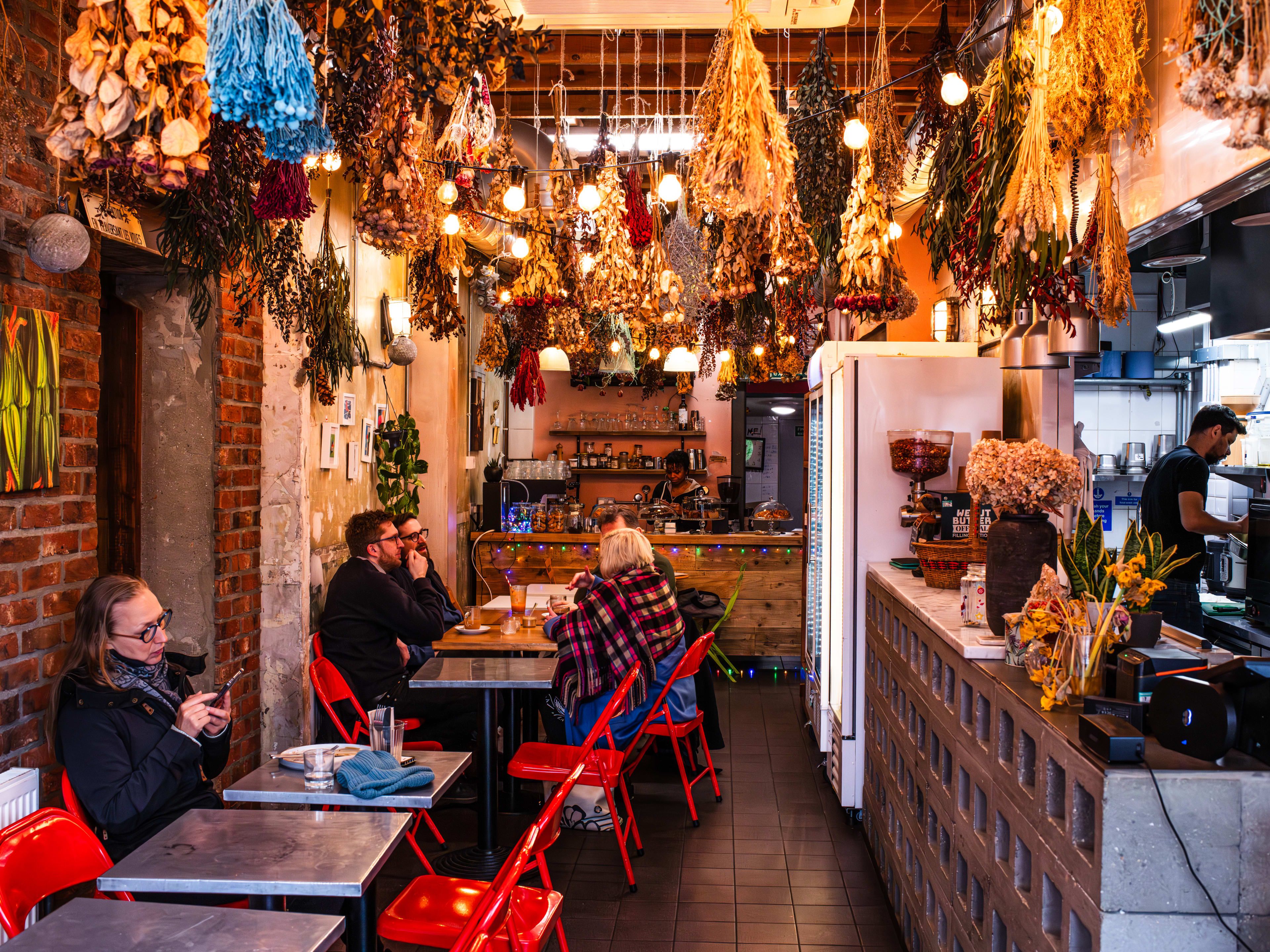 A cafe with dried flowers hanging from the ceiling, and a row of metal tables with red fold-out chairs.