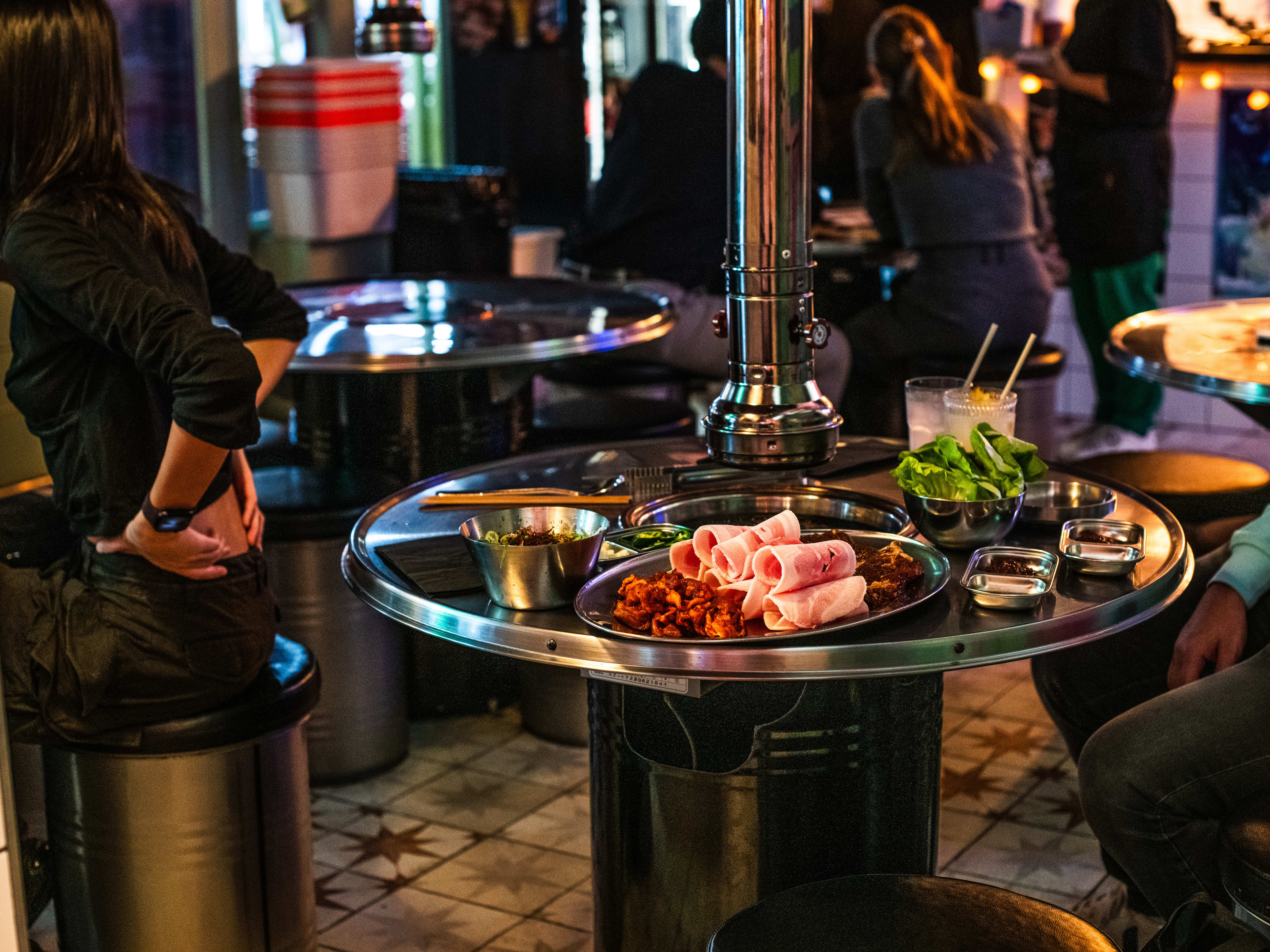 A spread of meats and veggies on a hightop table with a tabletop grill at Pochawa Grill