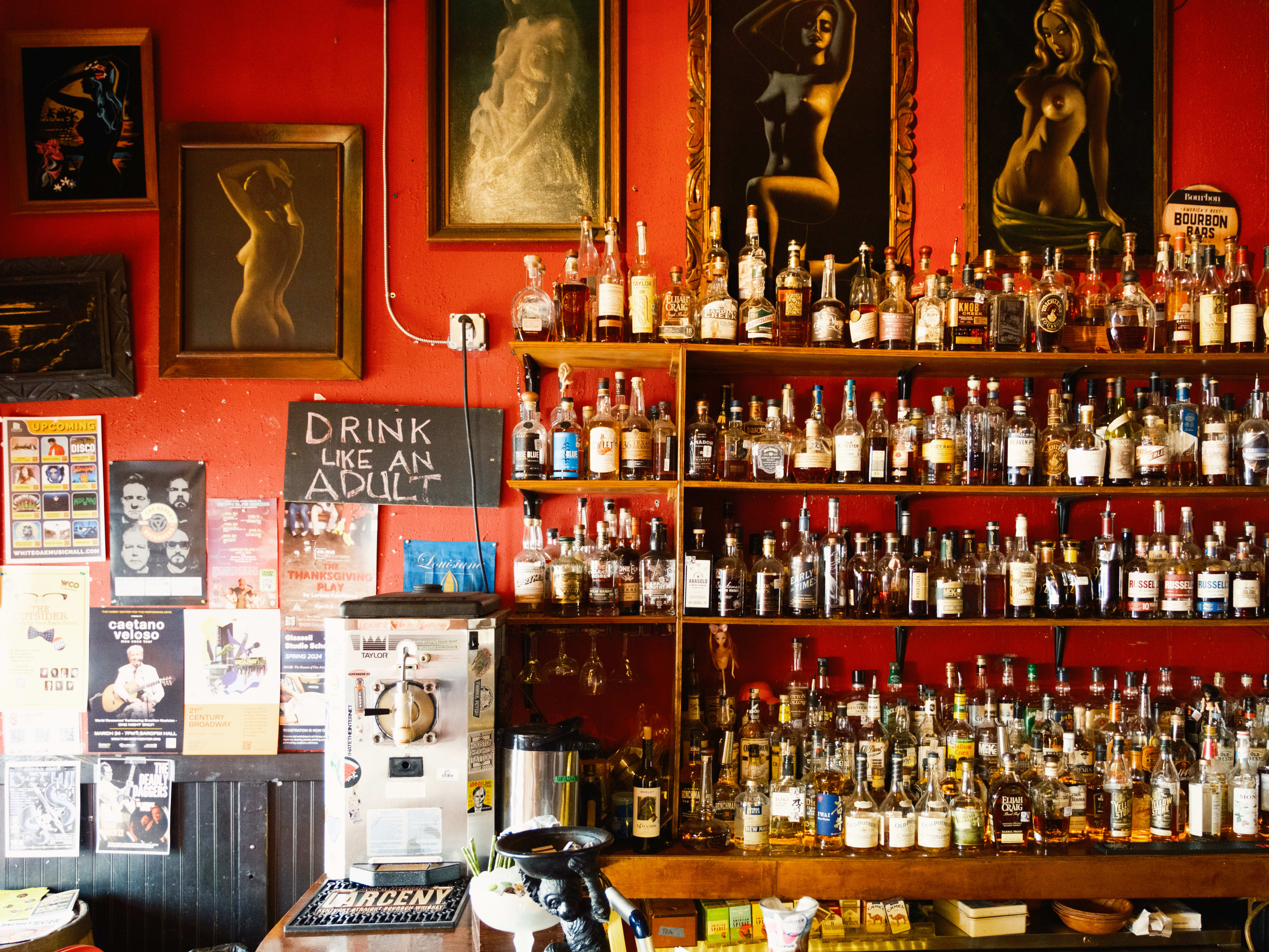 The bar at Poison Girl.  With framed nude paintings, a large whiskey selection, and posters on the red wall.