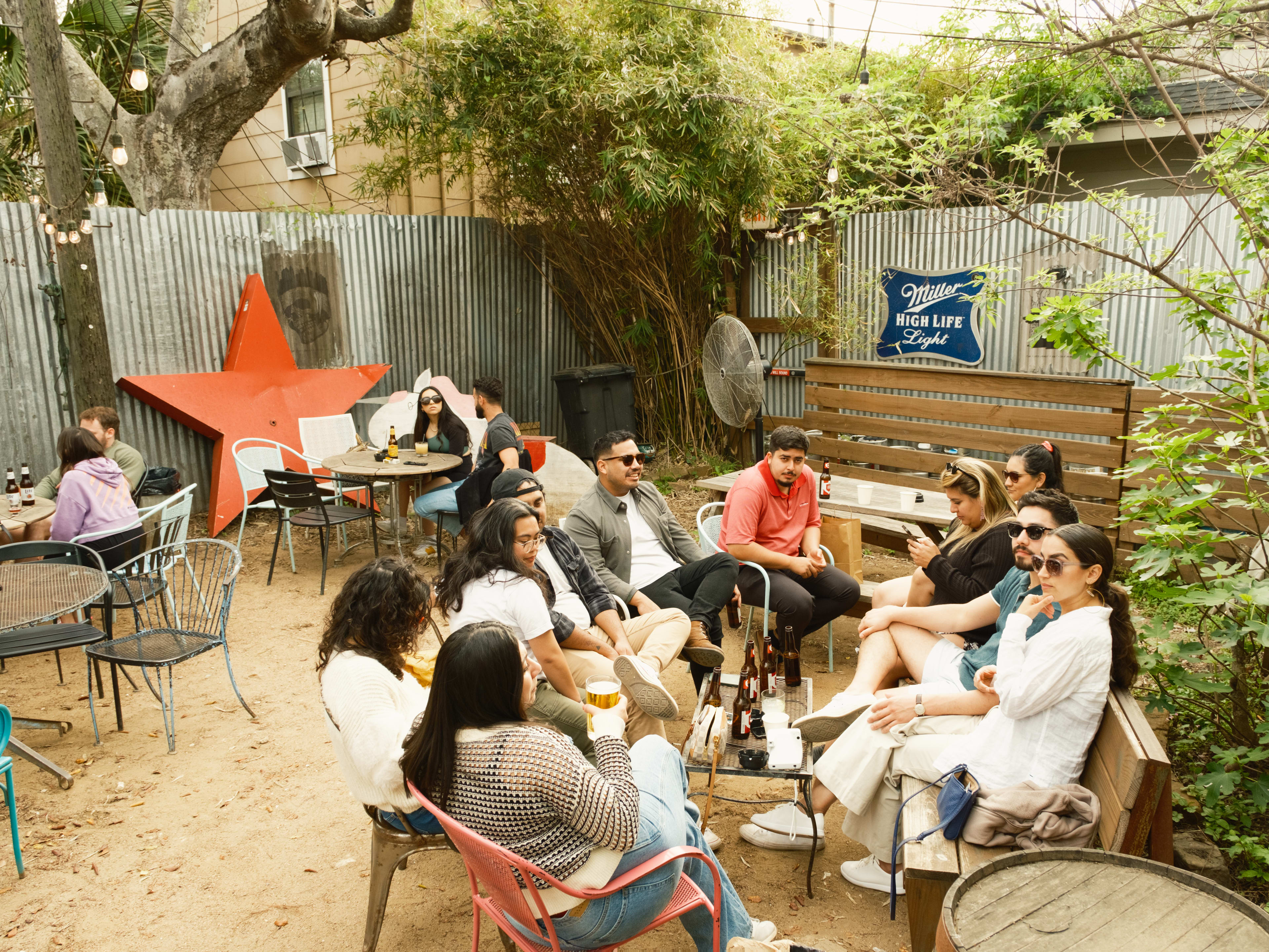 A group of people on the patio at Poison Girl. The ground is sand and there is a metal fence and hanging string lights.