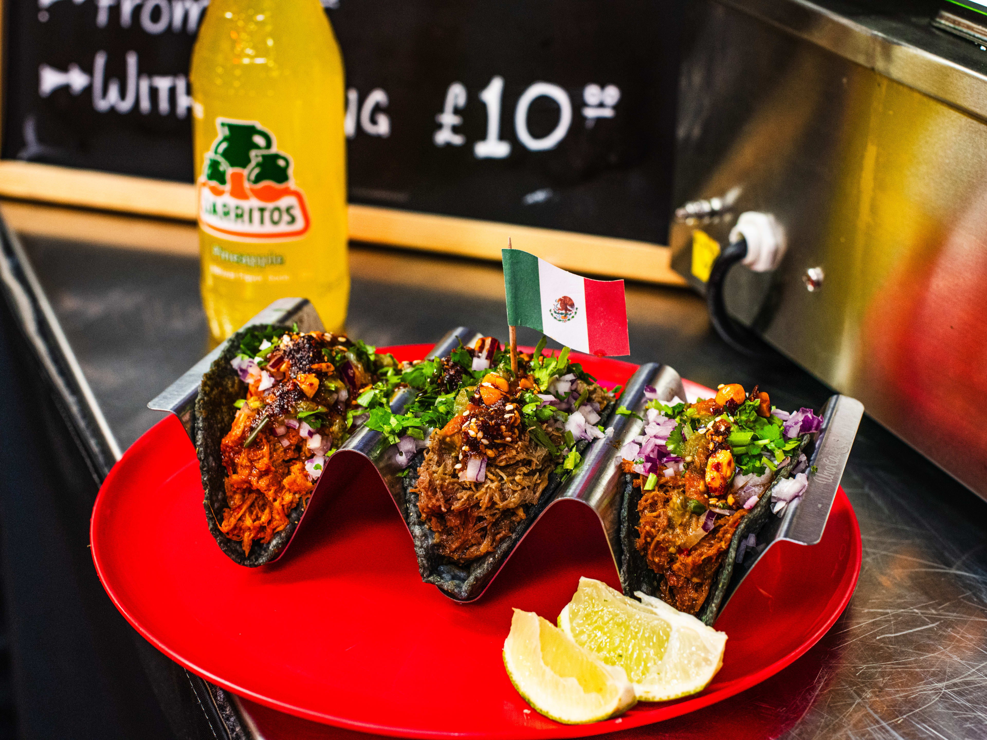 The carnitas, pulled chicken, and barbacoa tacos at Proper Tacos. Served in a taco tray, on a bright red plate, with a bottle of orange Jarritos.