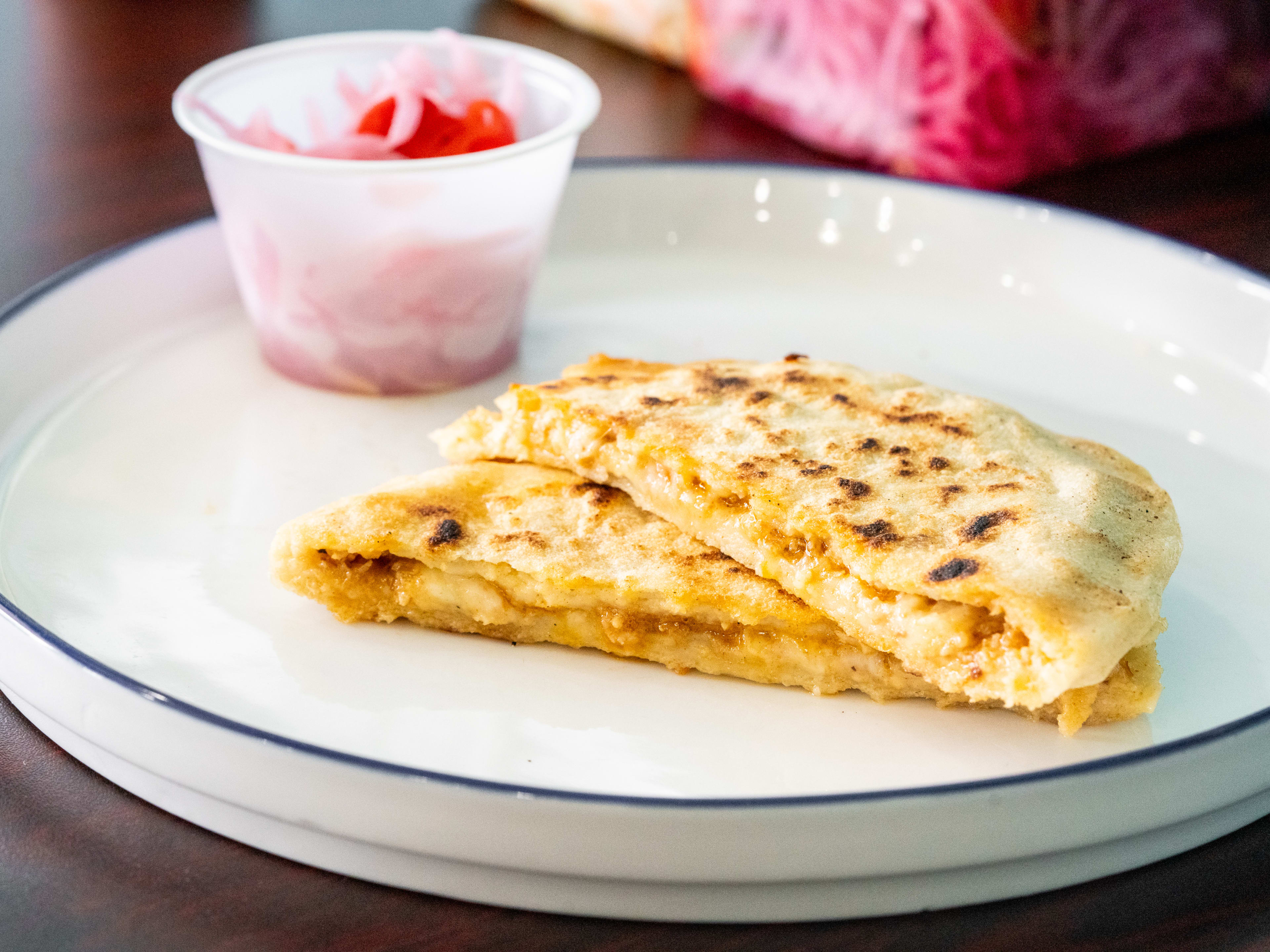 pupusa sliced in half to show filling next to small cup of pickled onions