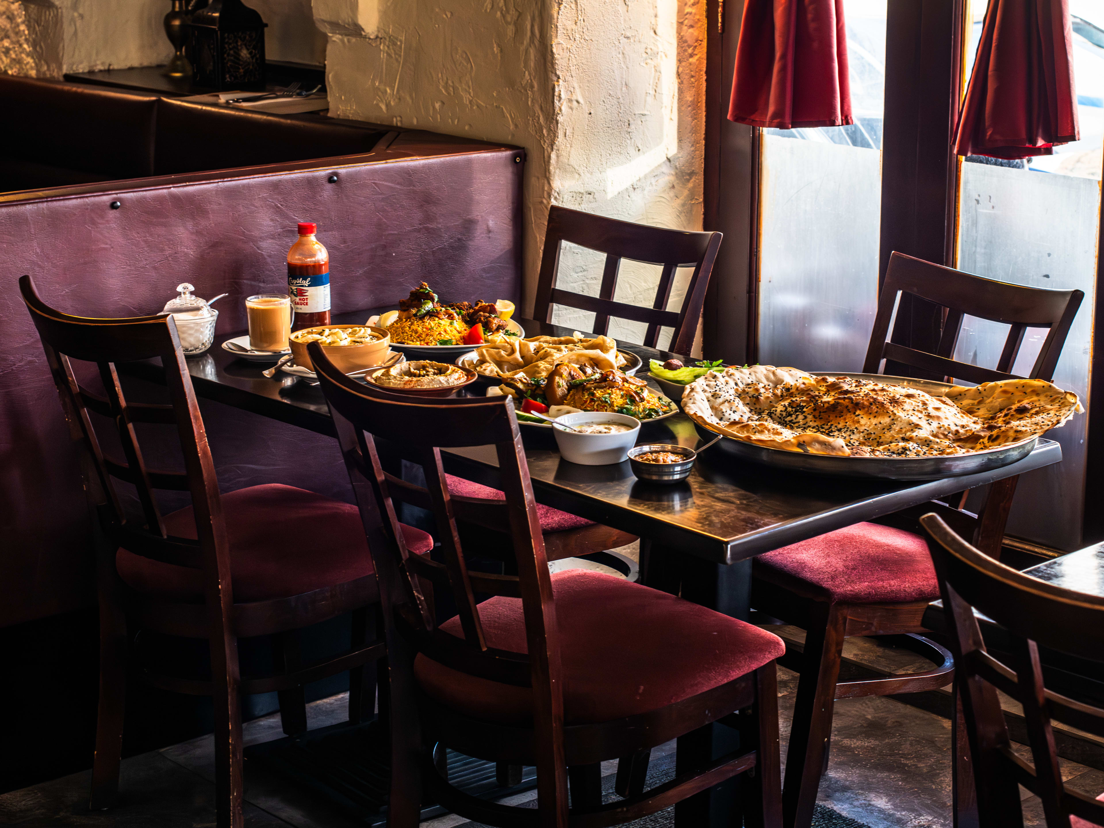 A spread of Yemeni food on a wooden table with four wooden chairs with red cushions.