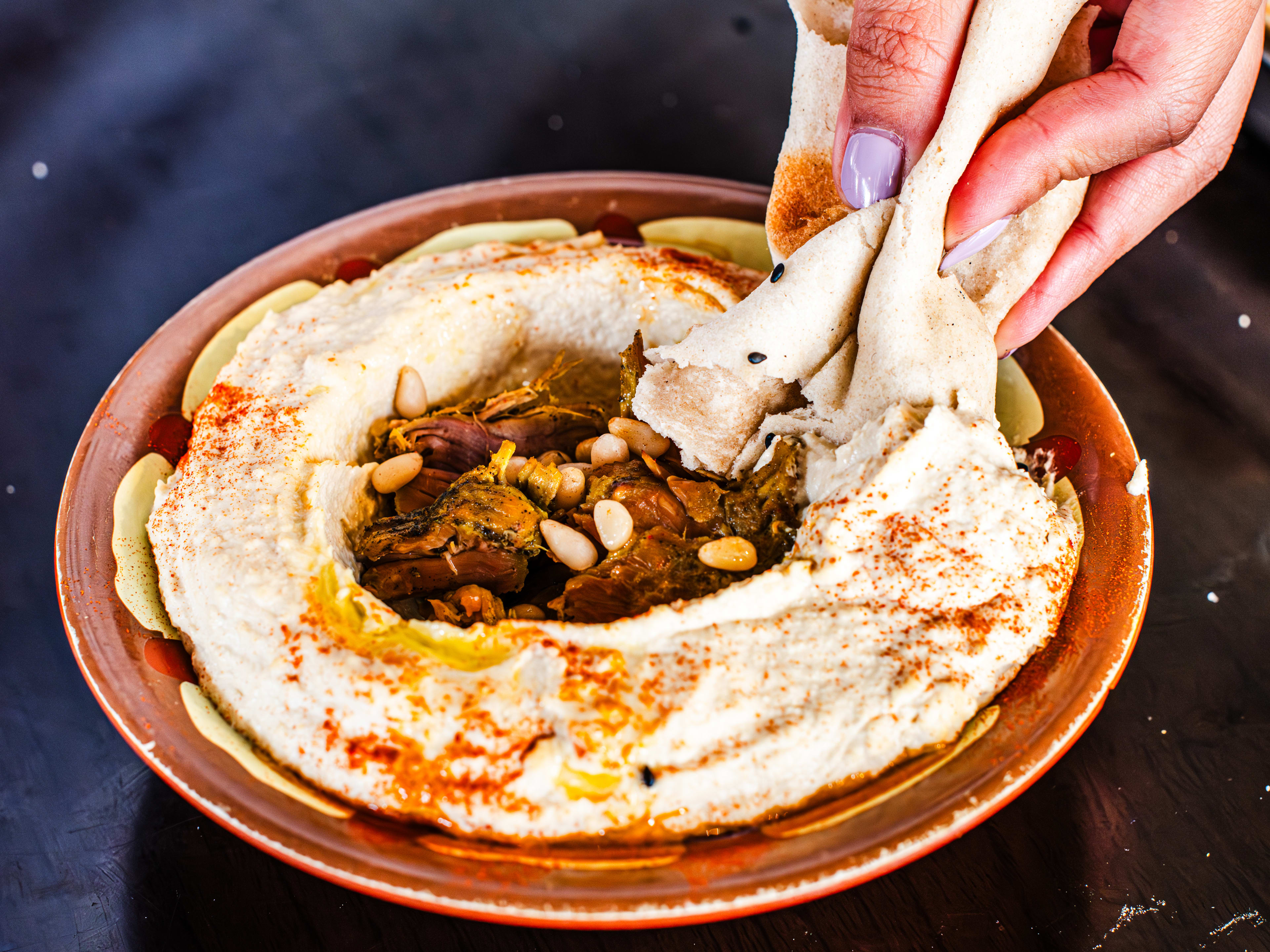 A hand scooping hummus with flatbread.