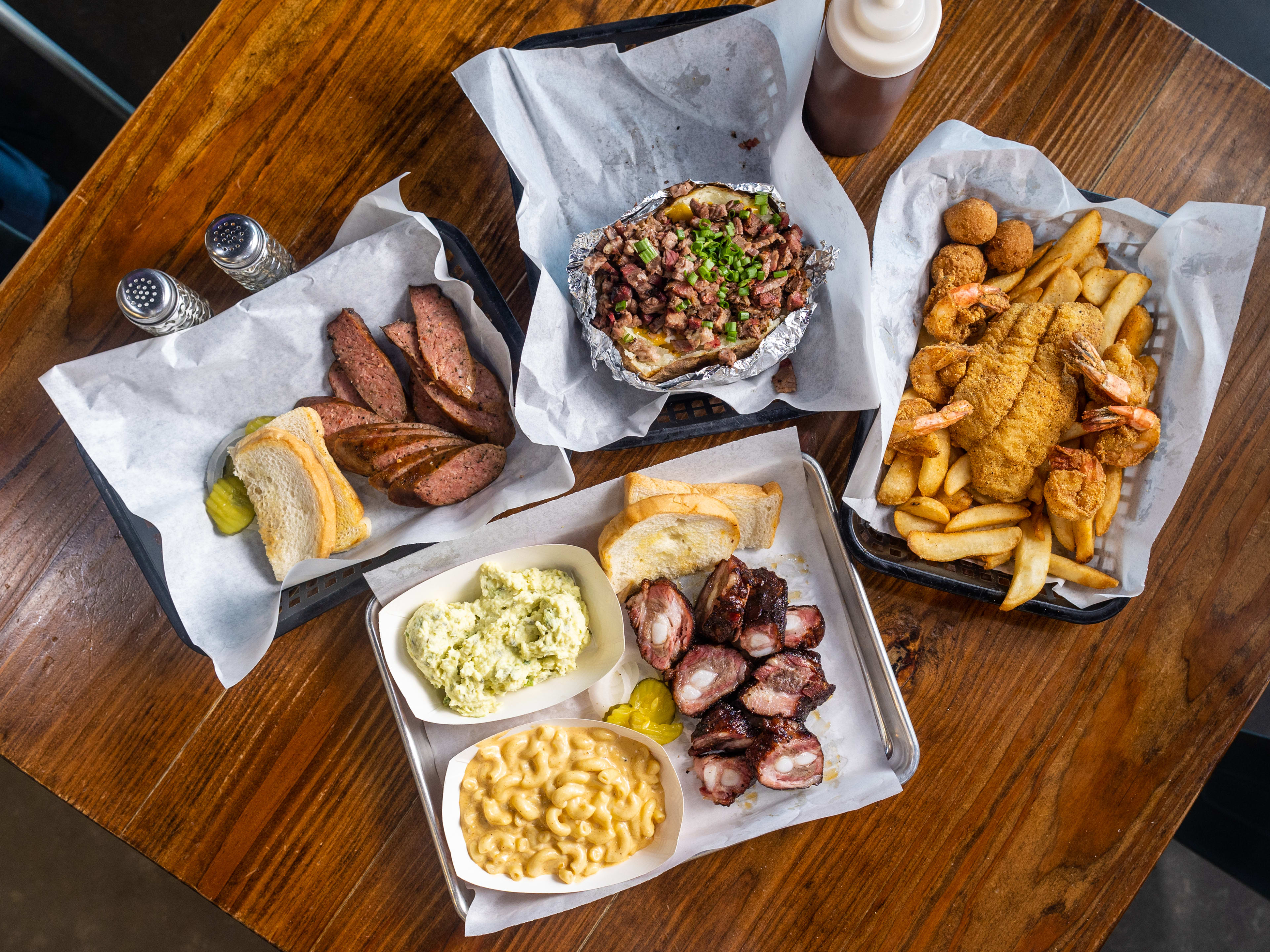barbecue spread on a wood table with smoked ribs, corn, french fries, and fried fish