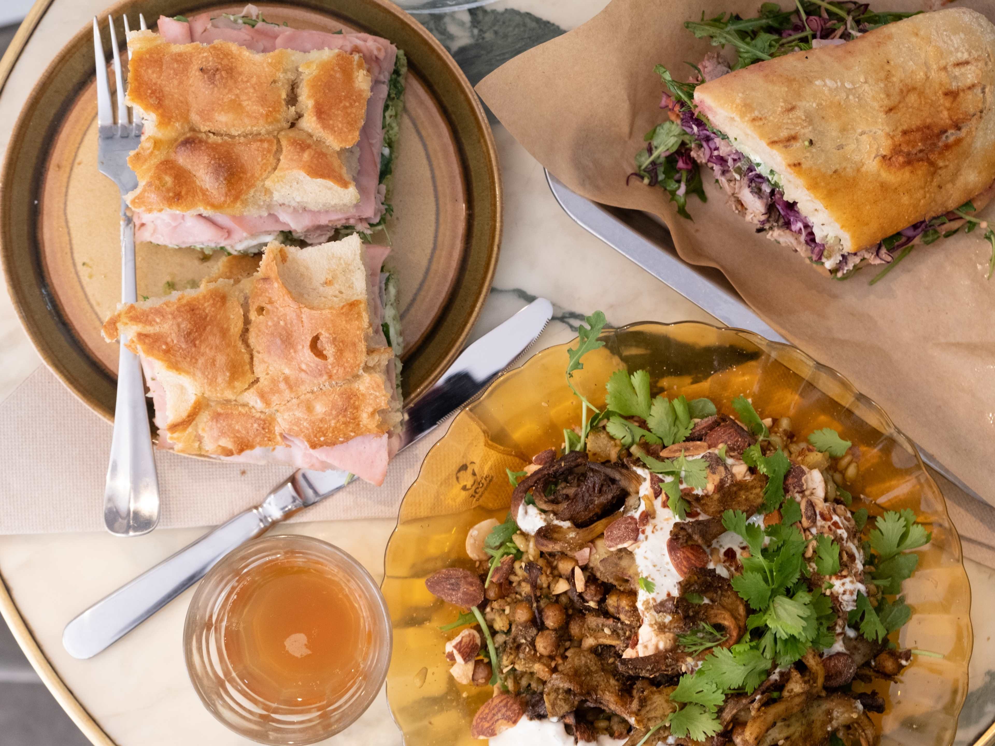 Sandwiches and other plates of food on a table with a glass of wine