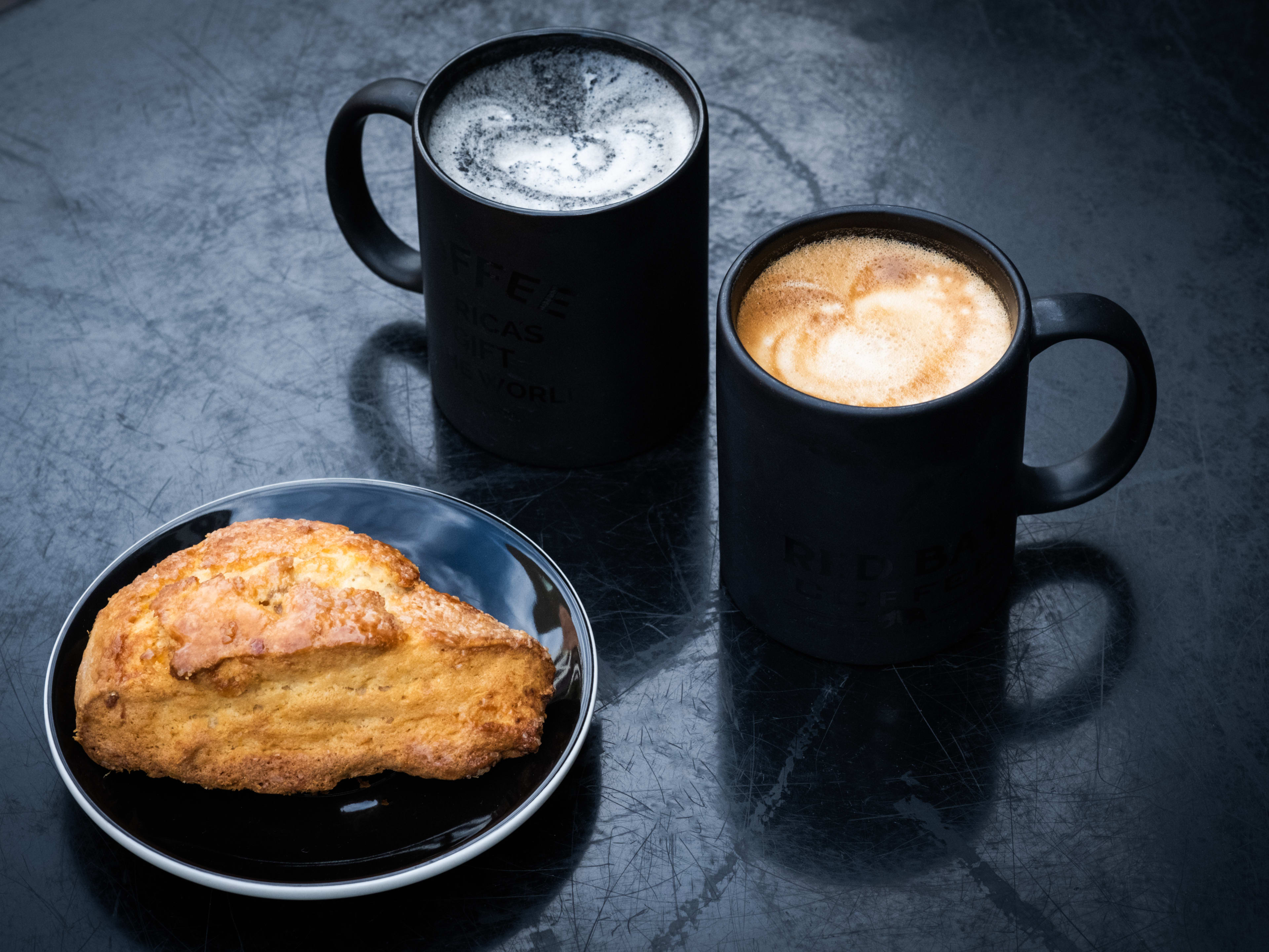 scone on plate and two mugs of hot latte