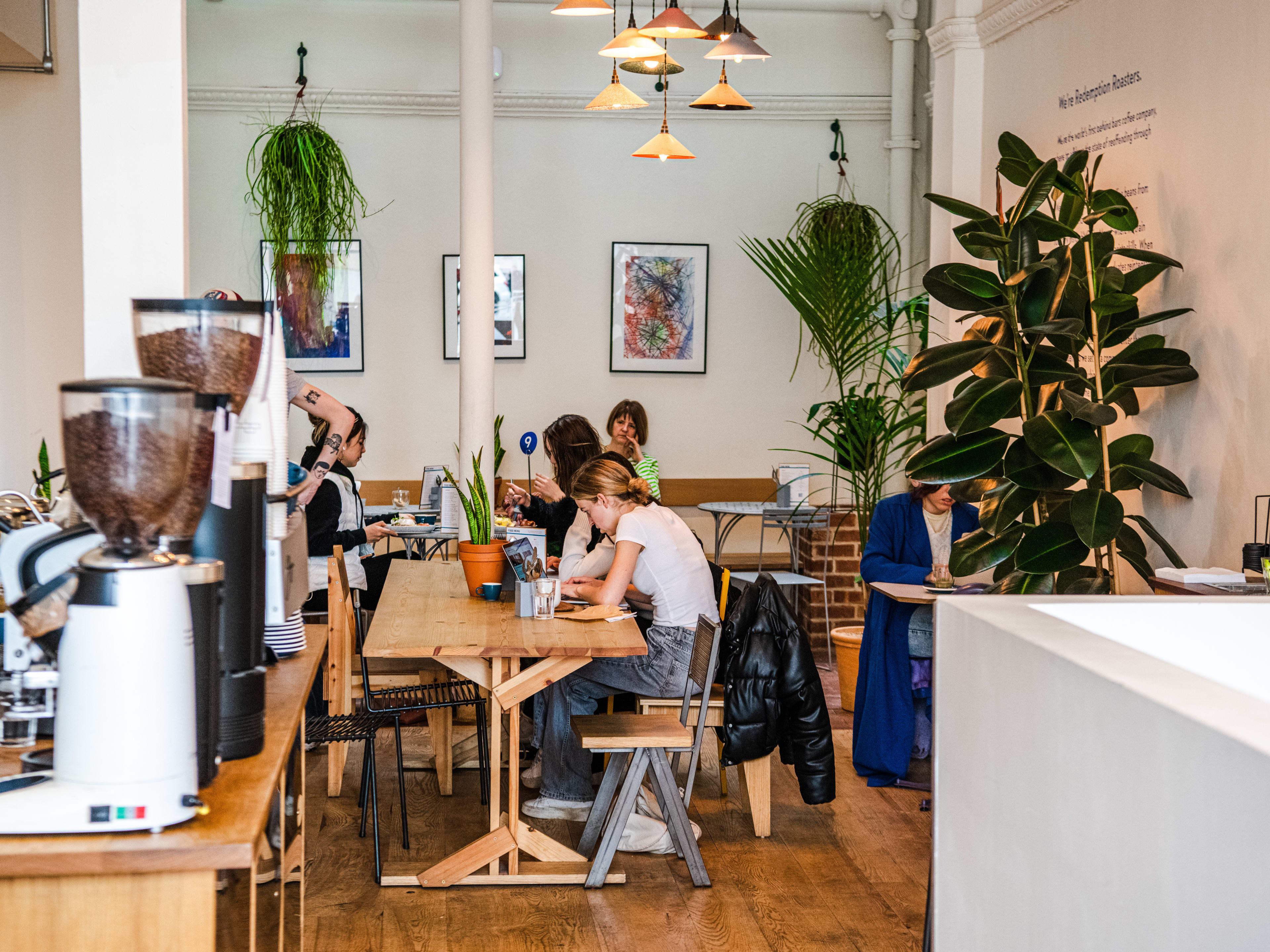 The airy interior of Redemption Roasters. There are large plants, and people working at tables.