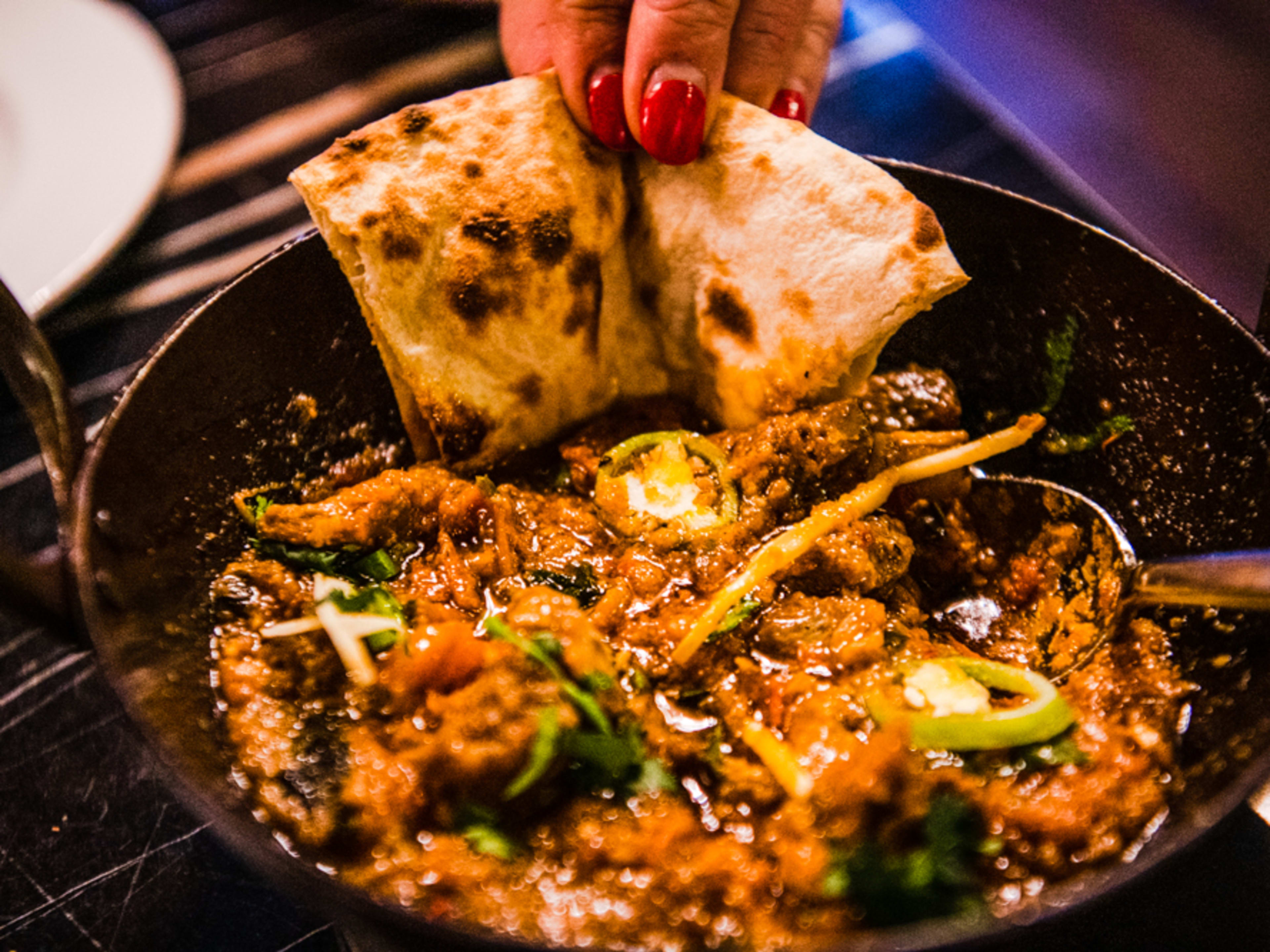 Dipping naan into a skillet of lamb handi