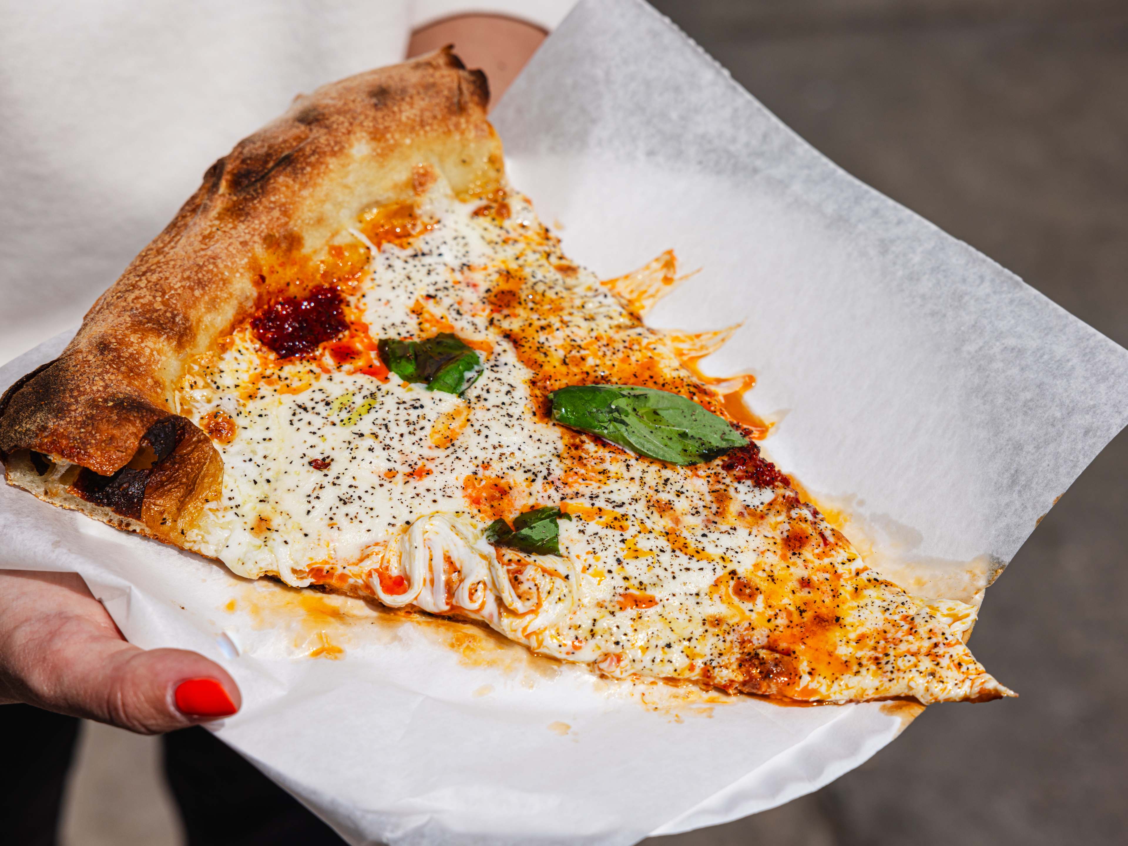 Two hands holding a slice of pizza on a paper plate.