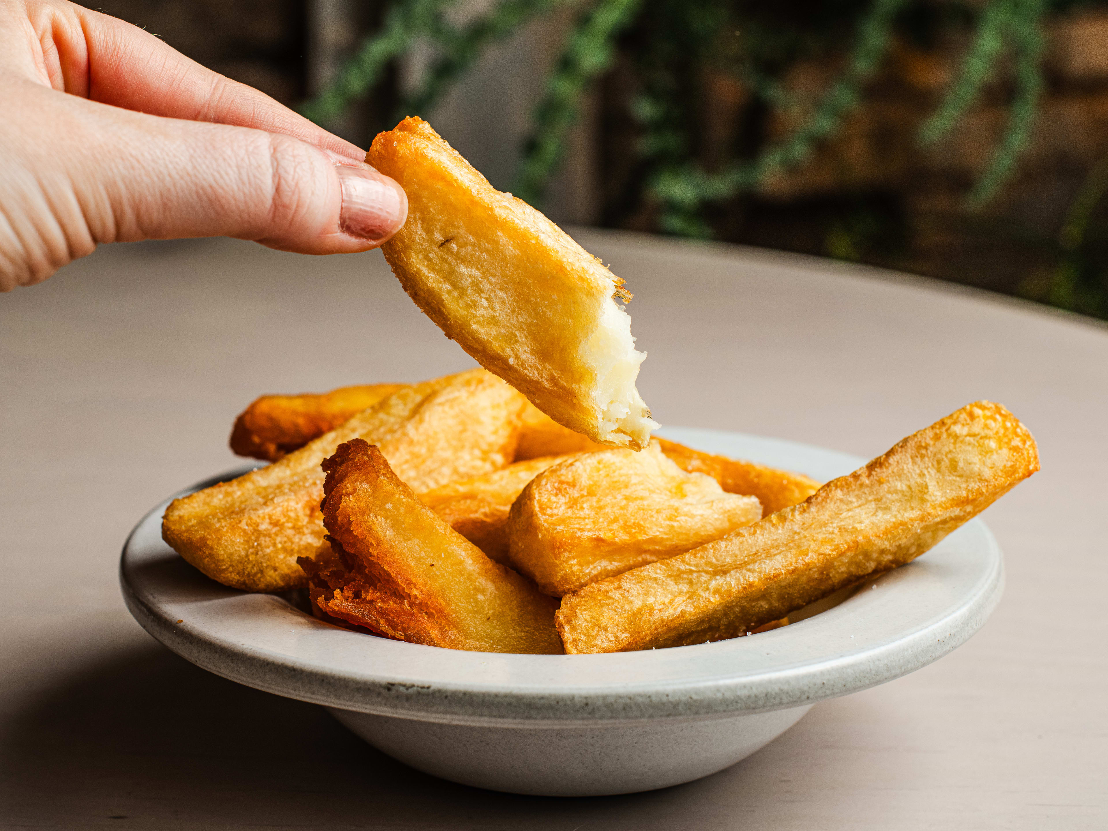 Person holding up half a chip from a small white dish of chips.