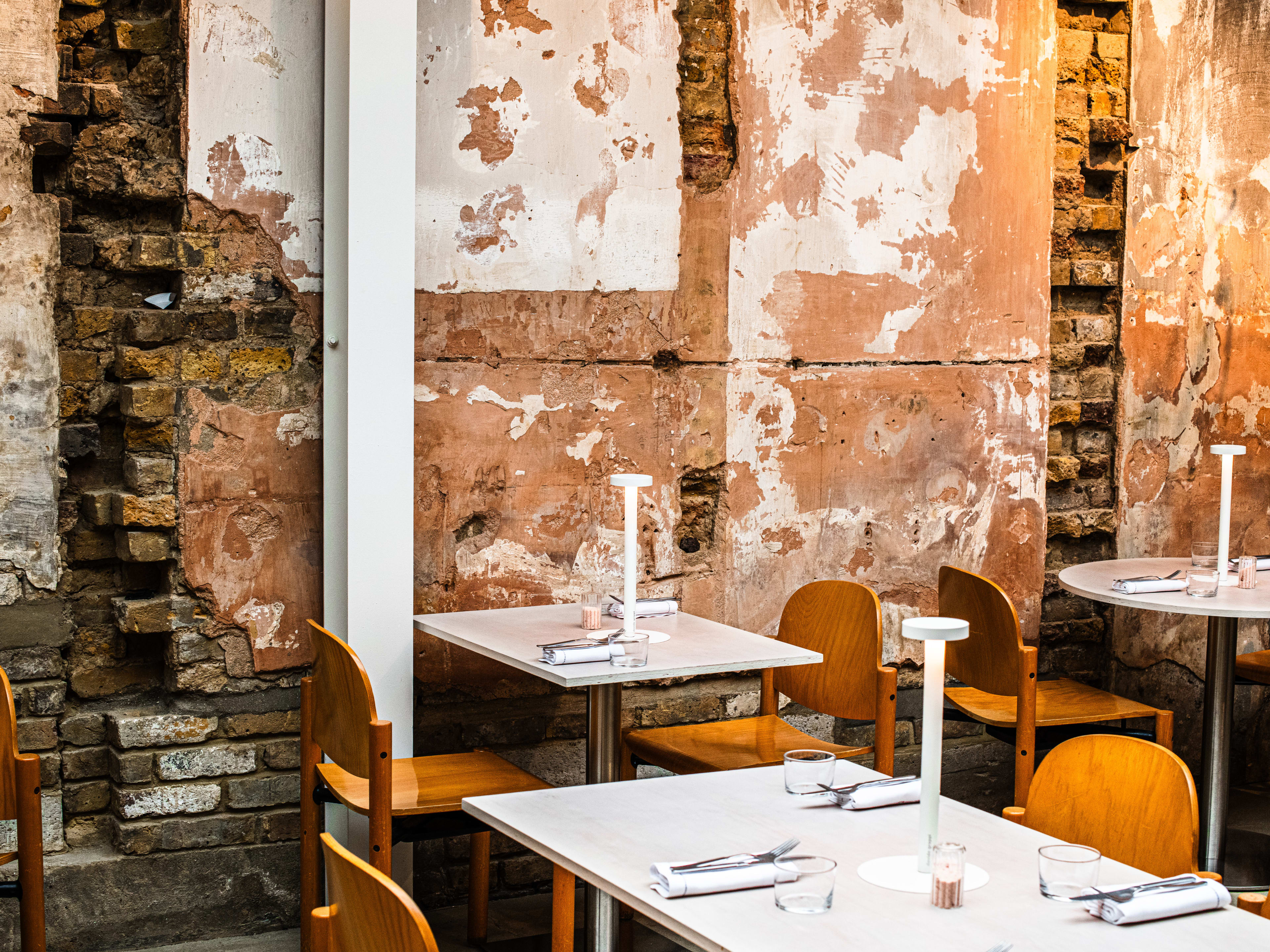 The interior of Saltine with distressed walls revealing a brick underlay, white tables and modern wooden chairs.