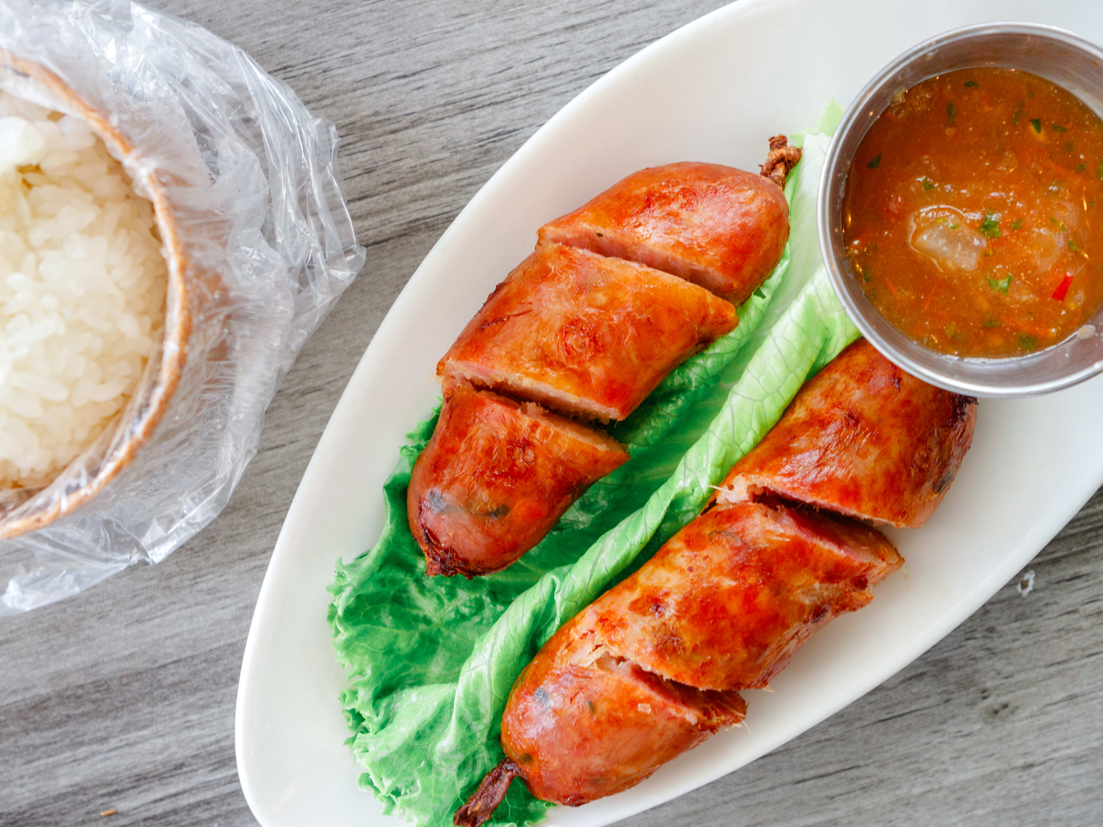 sliced thai sausage links with a side of sauce and sticky rice