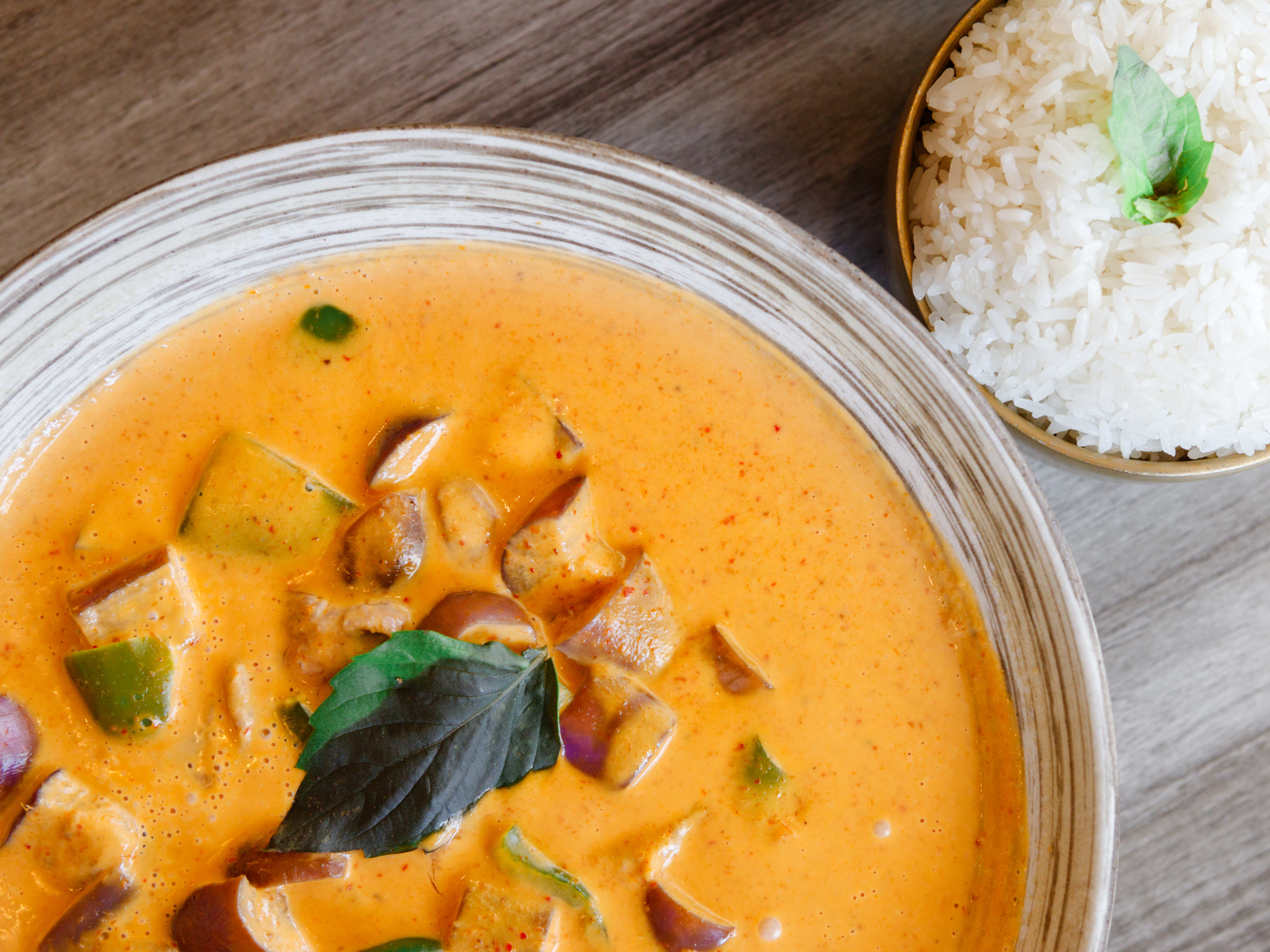 bowl of orange-red thai curry with sliced ribeye, eggplant, and white rice