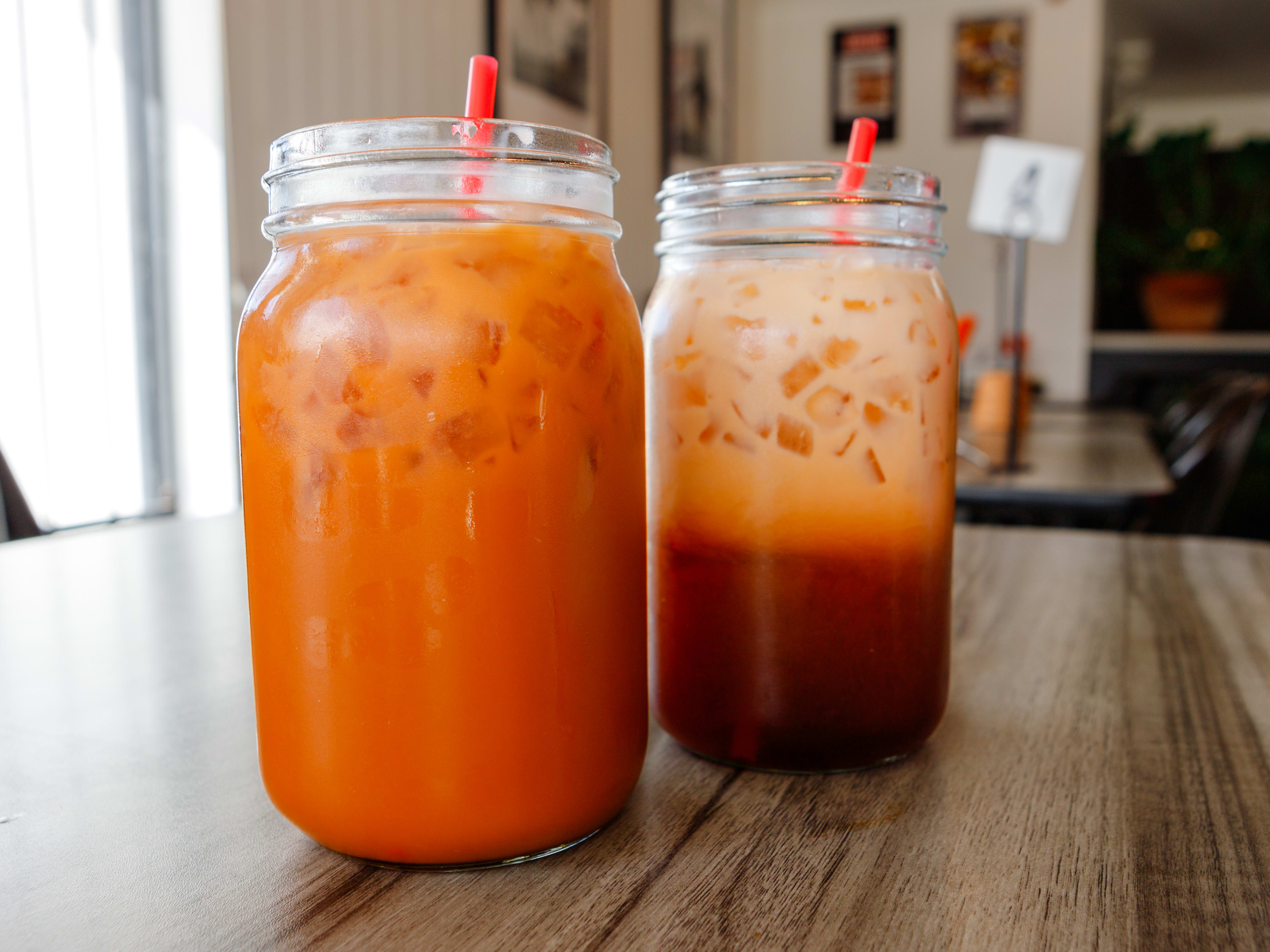 Two Thai iced teas served in mason jars with red straws.