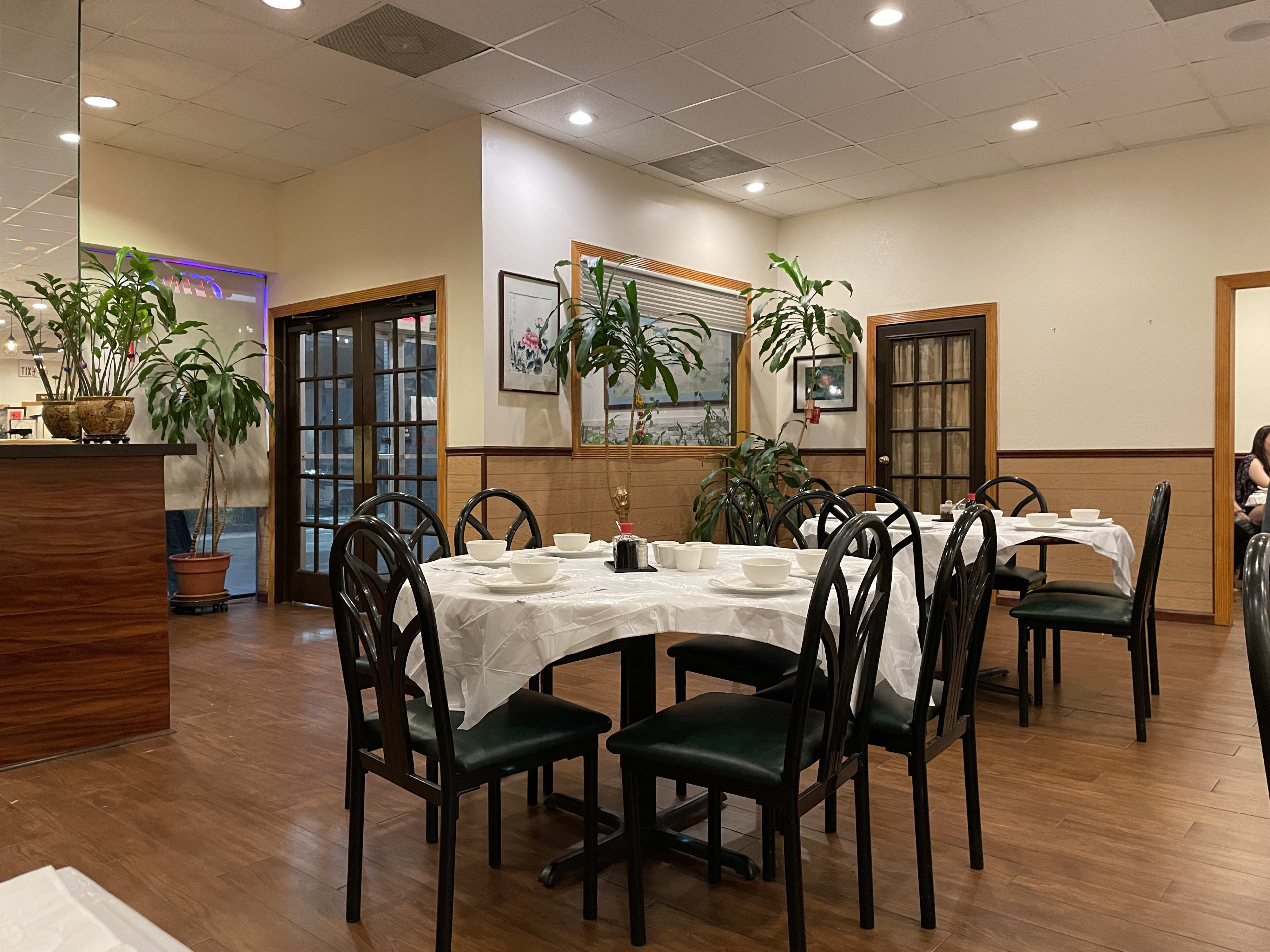 Restaurant interior with tropical plants, black chairs, and white tablecloths