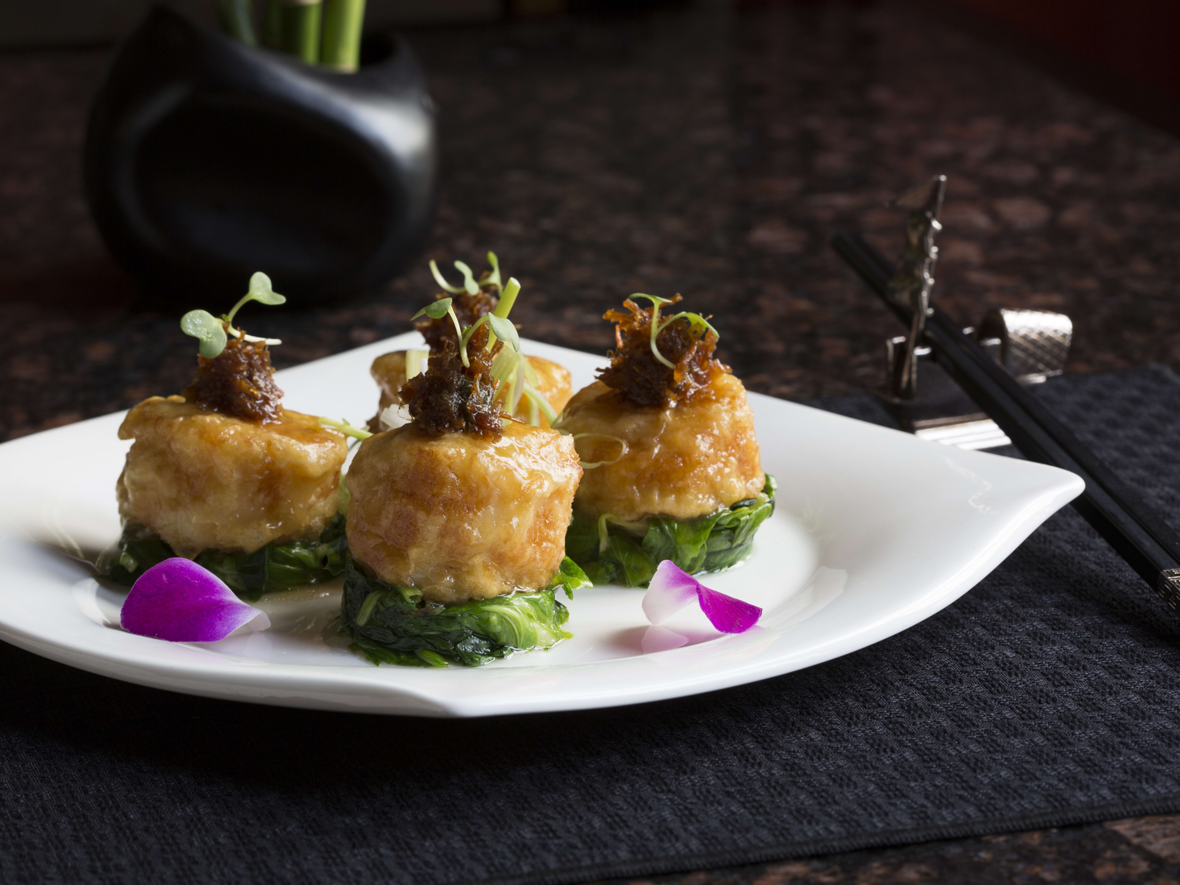 Plate of three XO scallops lined up with complex garnishes and two flower petals