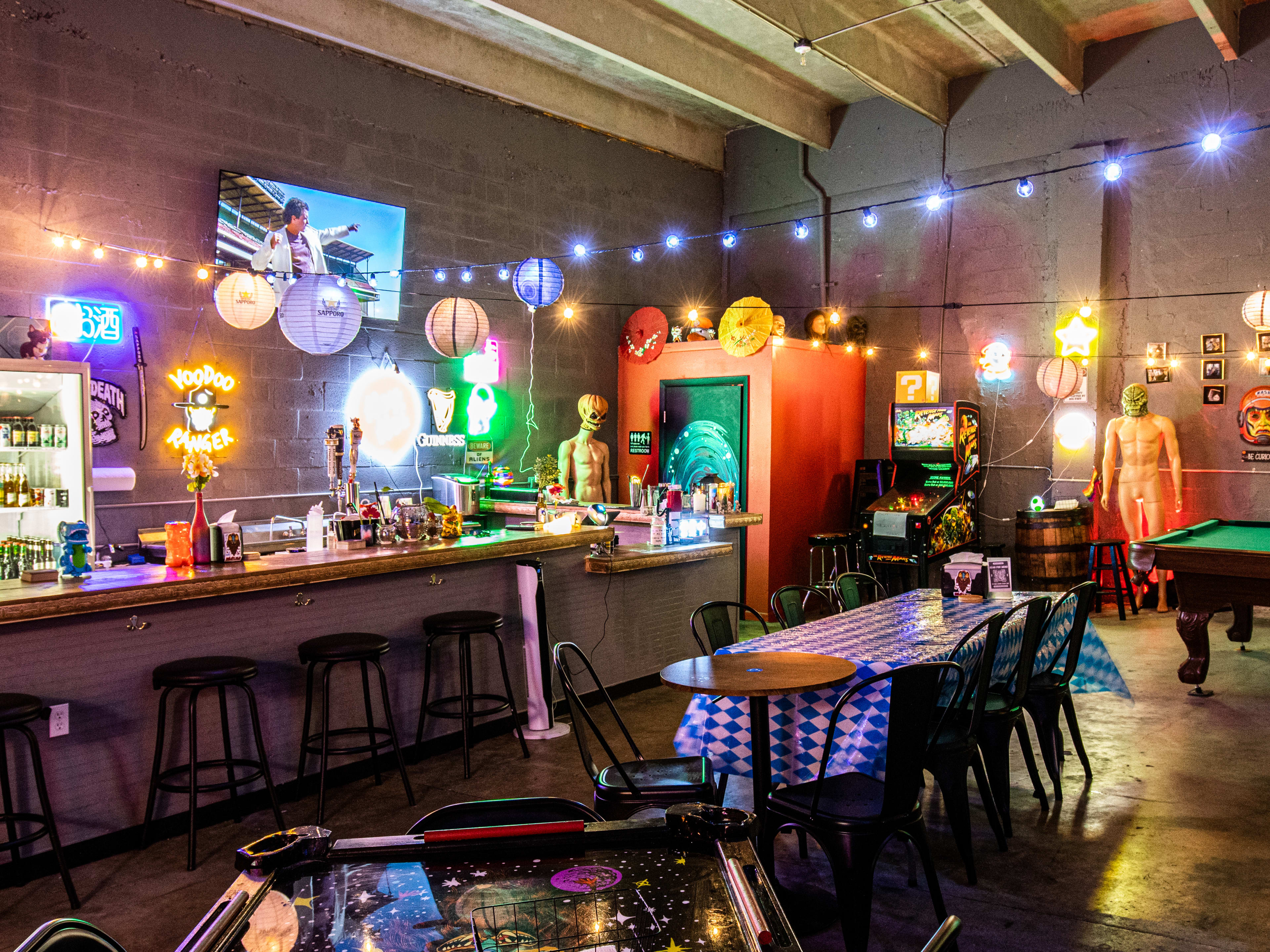 A bar in a warehouse with string lights and alien statues.