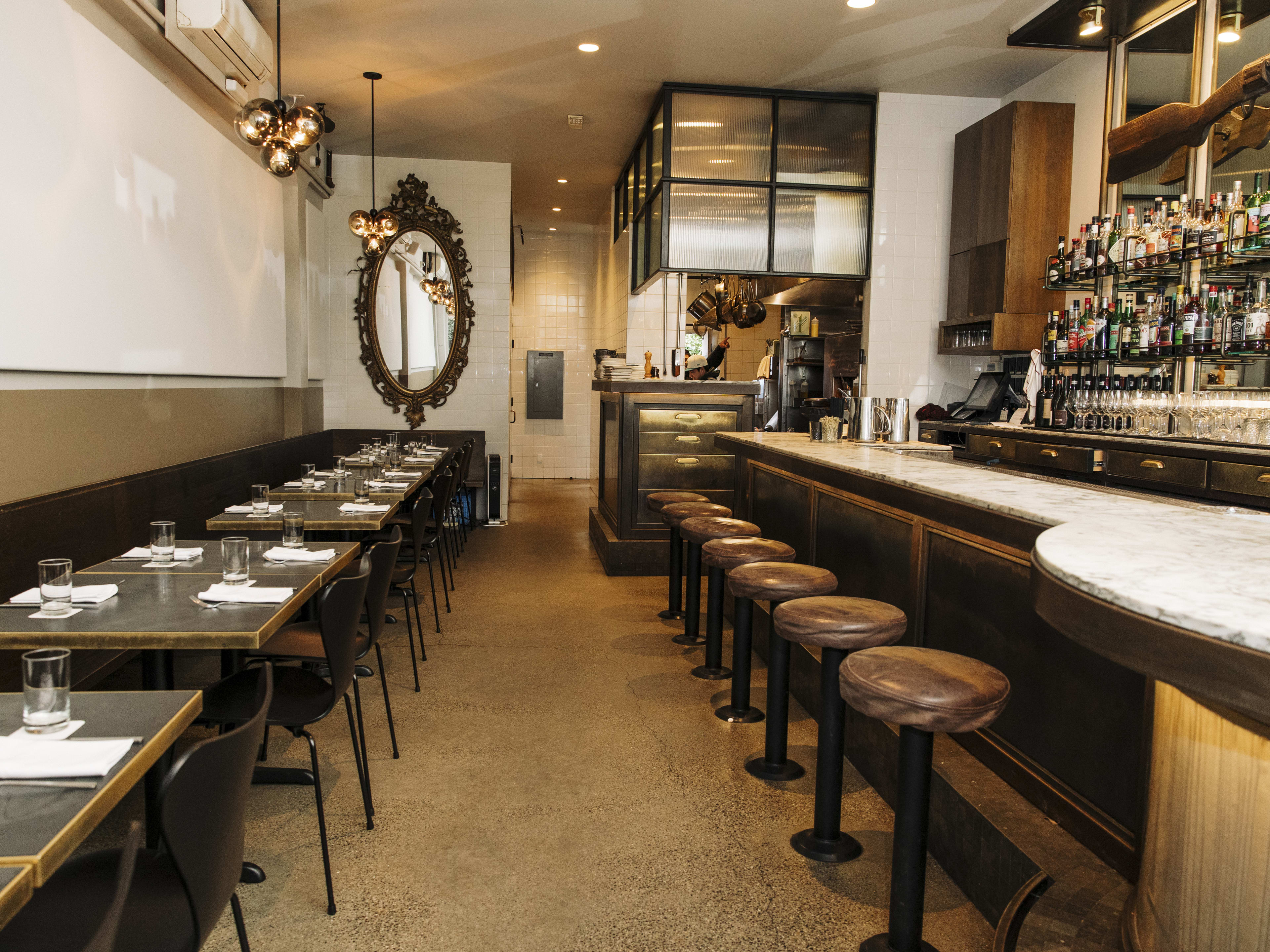 A narrow dining room with a marble bar, leather barstools, and a few tables and chairs.