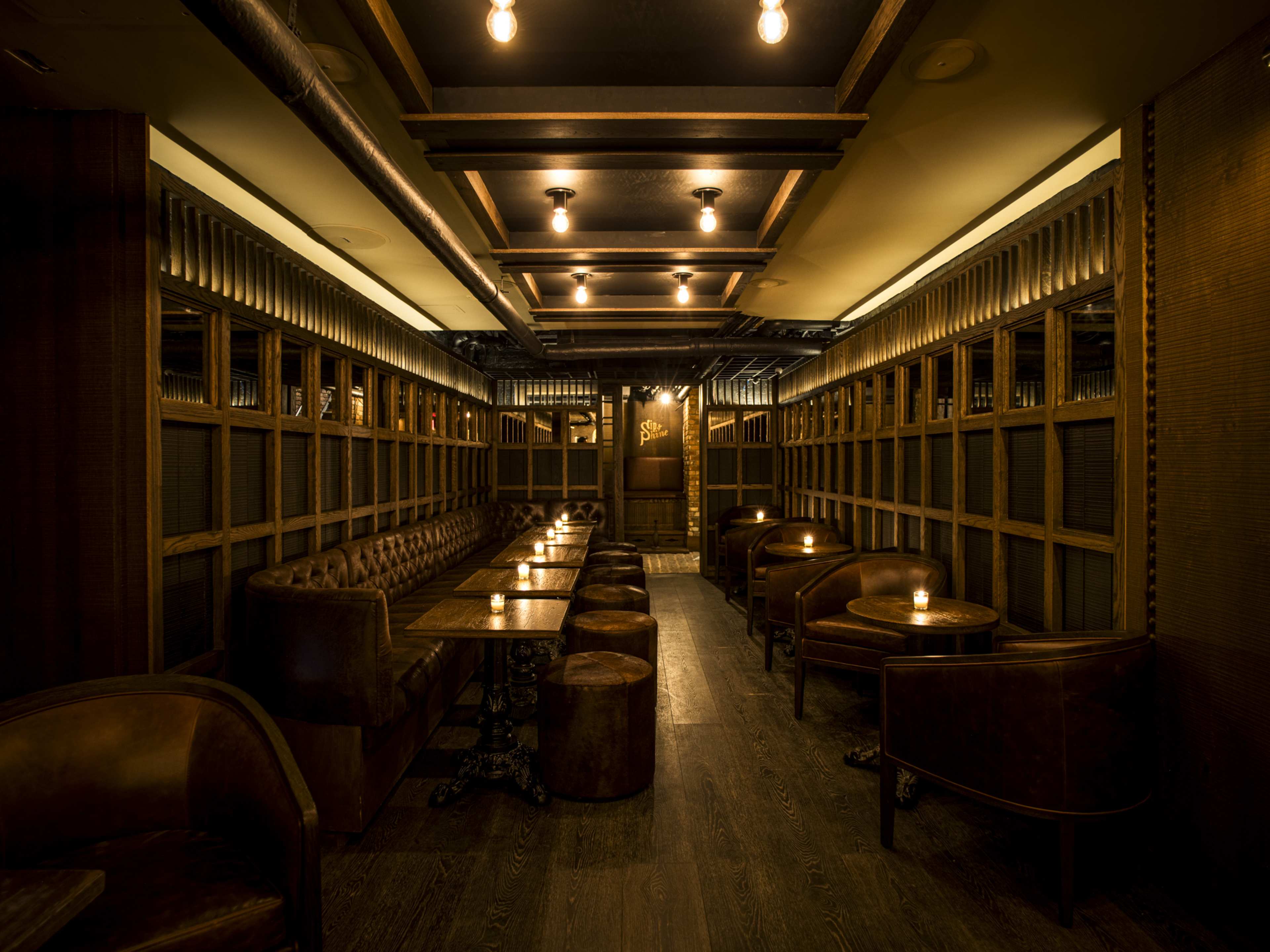 A dark bar with wood walls and candles on the tables.