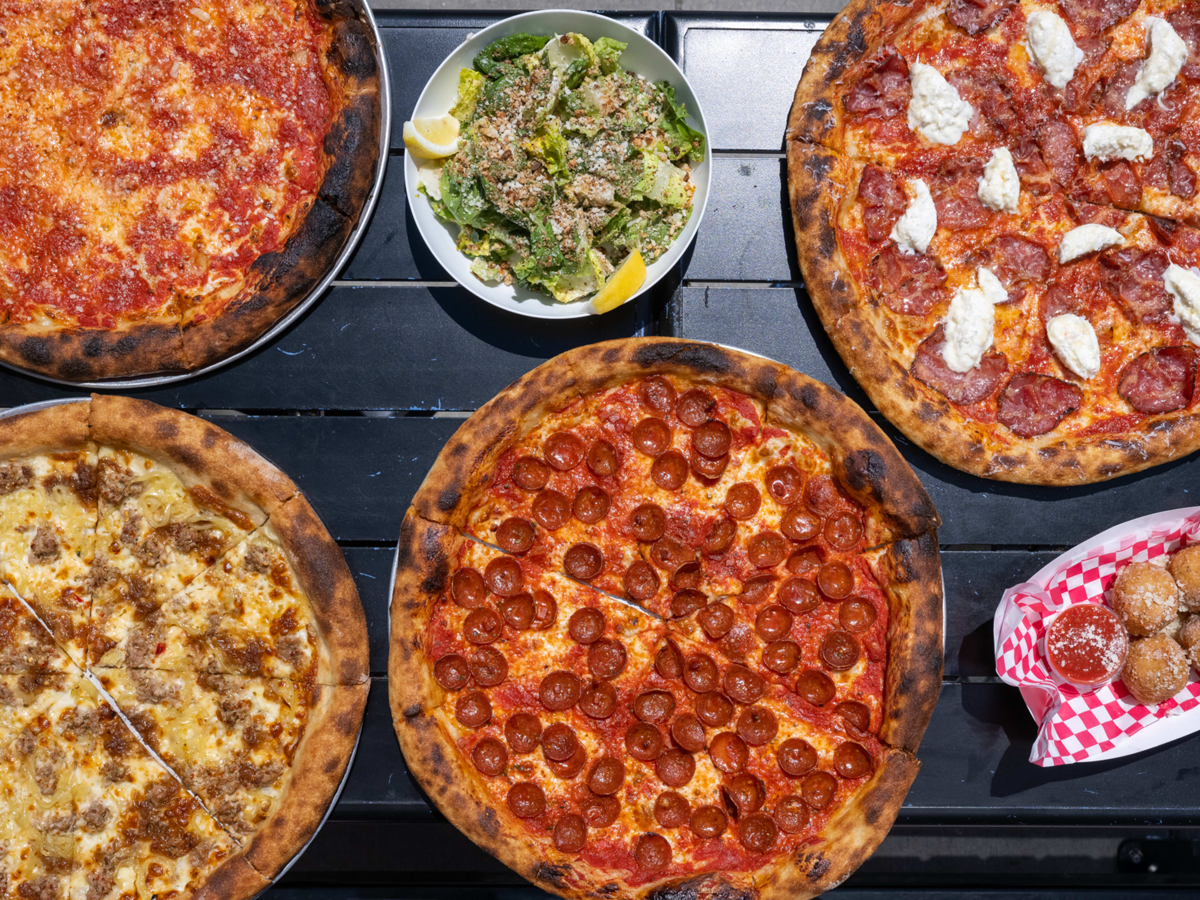 Spread of pizzas, along with a salad and arancini