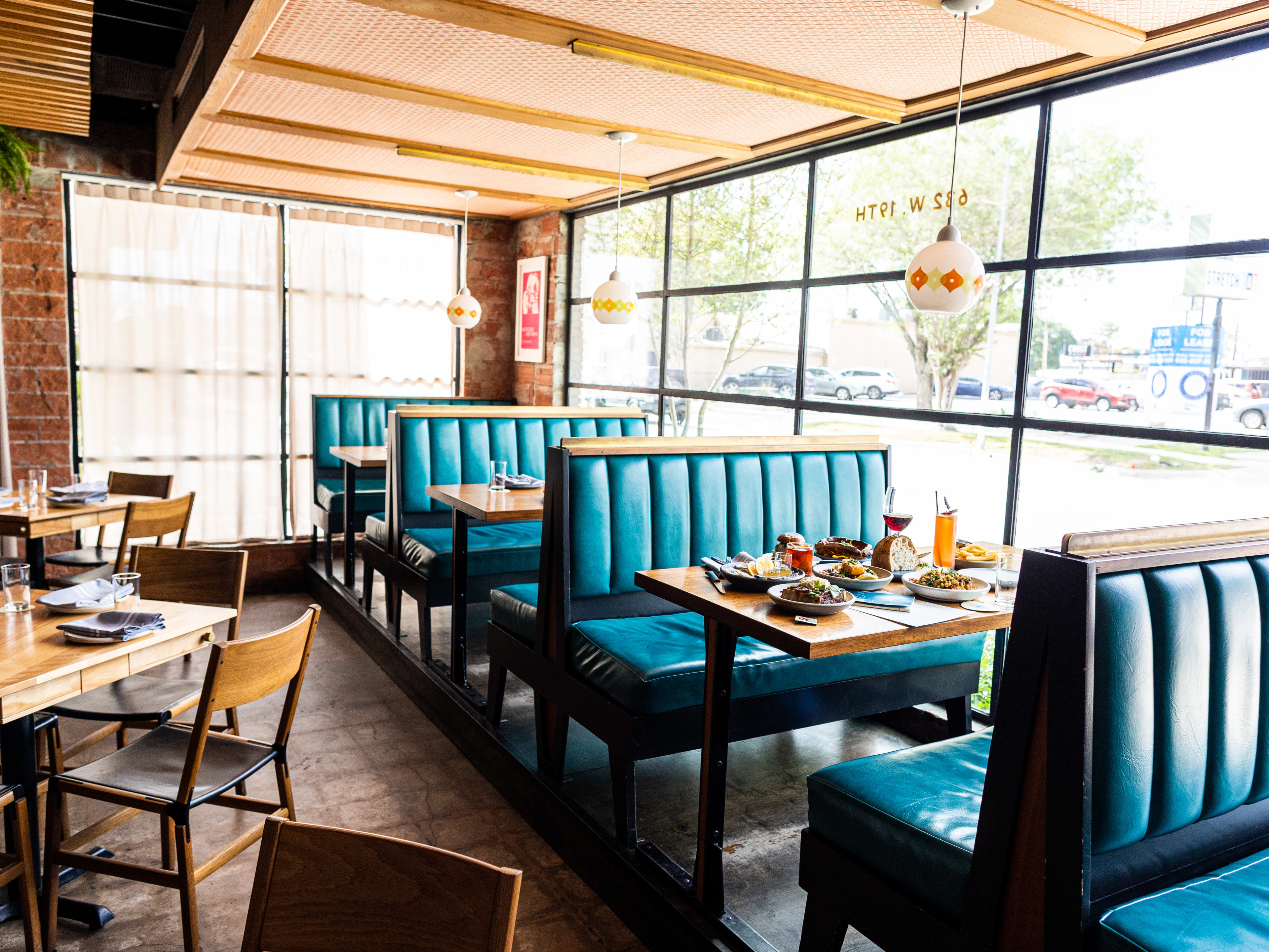 The interior of Squable with teal booths, smaller wooden tables, and large windows.  A spread of various dishes are set on one of the booths' tables.