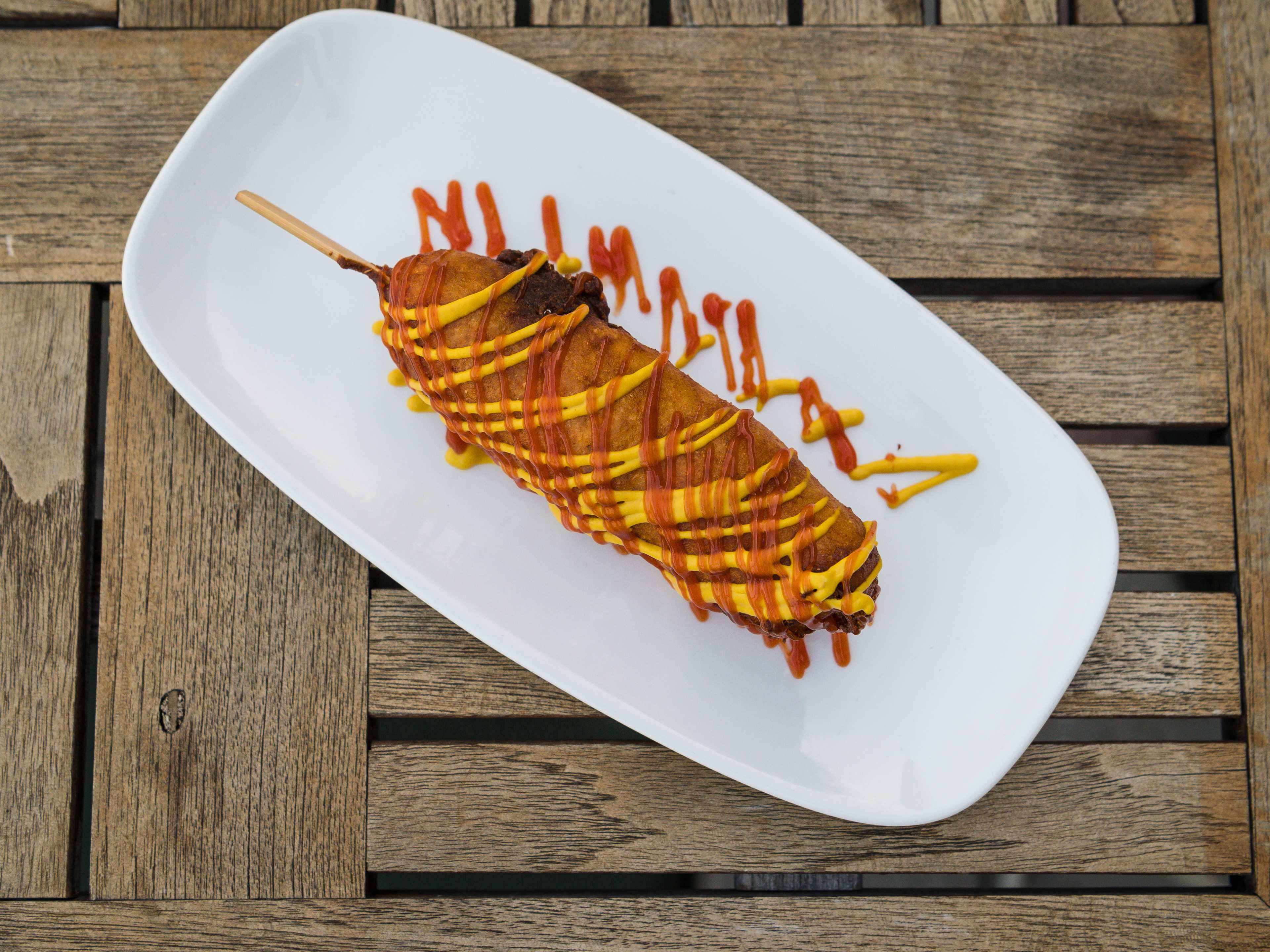 A corn dog with mustard and ketchup drizzled on top.