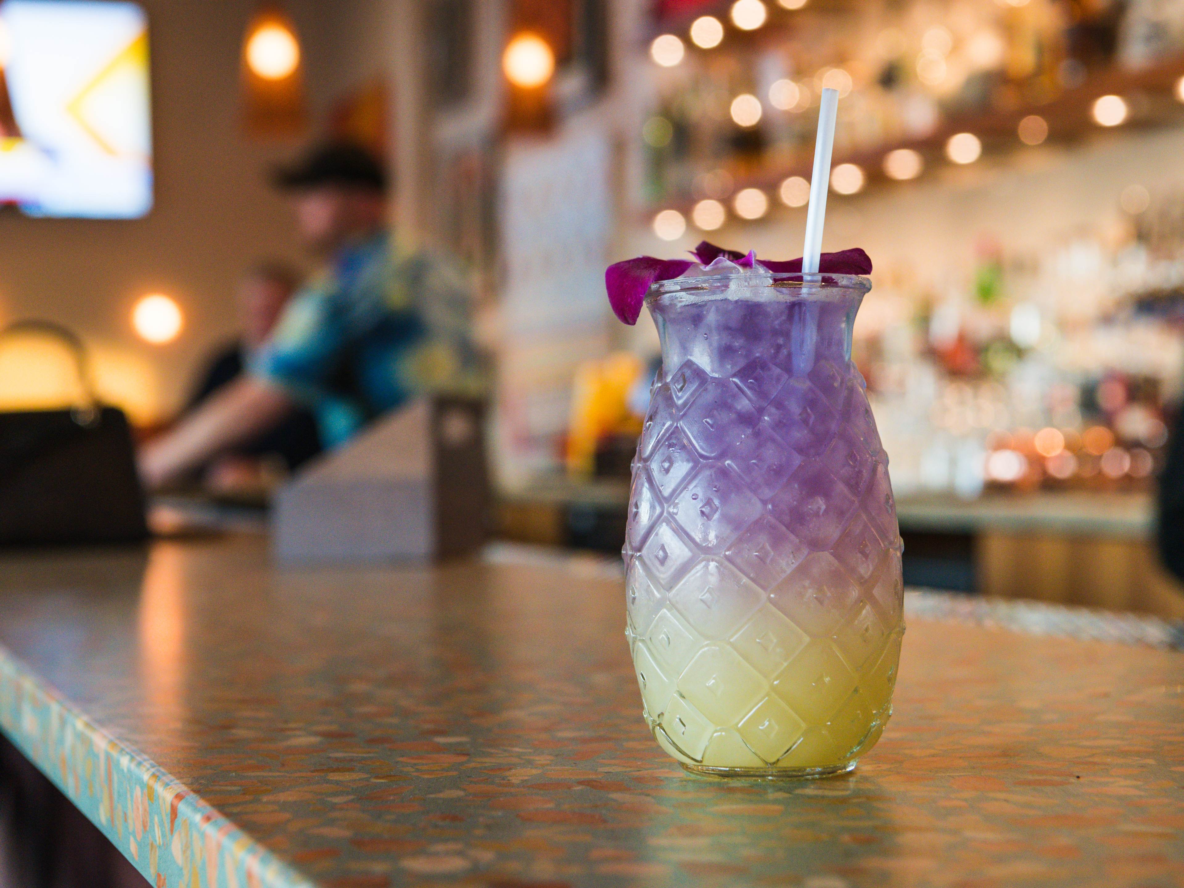 A purple and yellow cocktail with a purple flower.