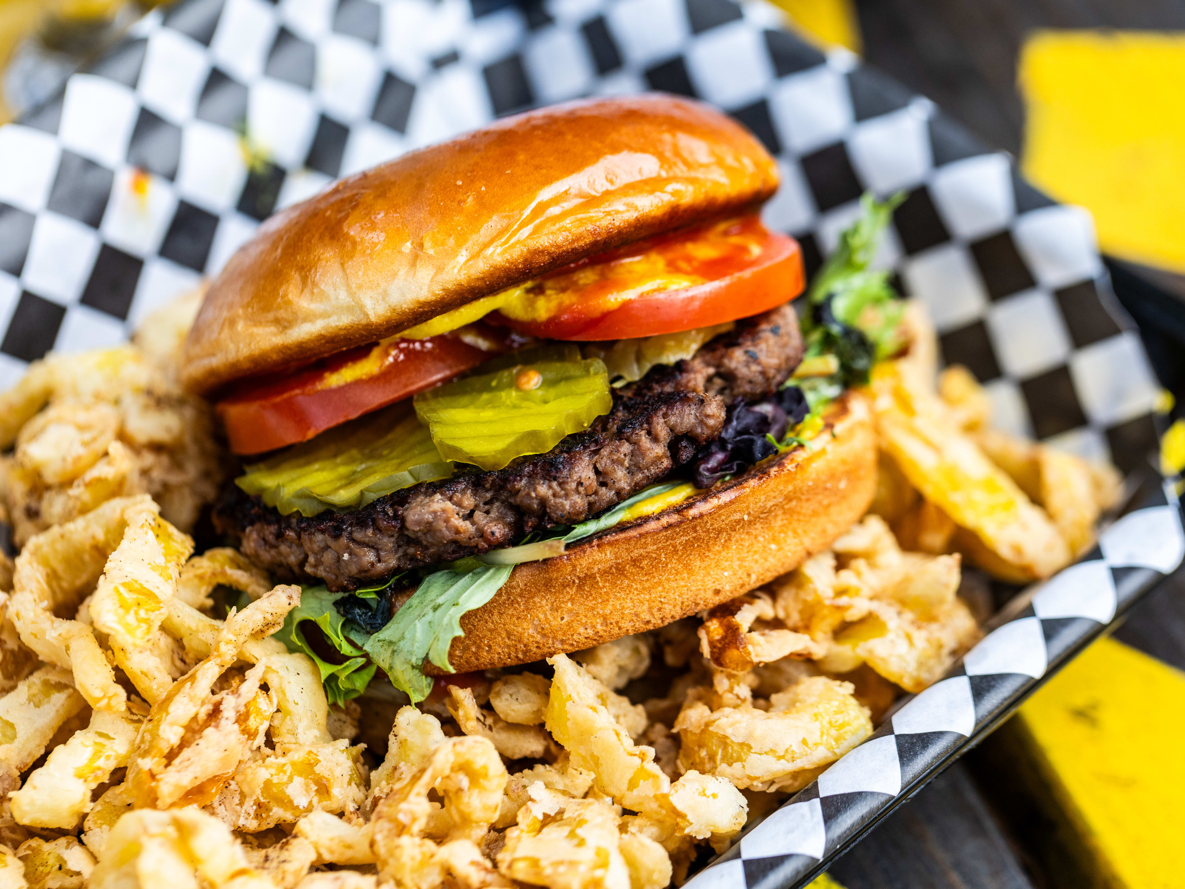 A Backyard Burger in a black and white checkered paper lined basket with fried banana peppers